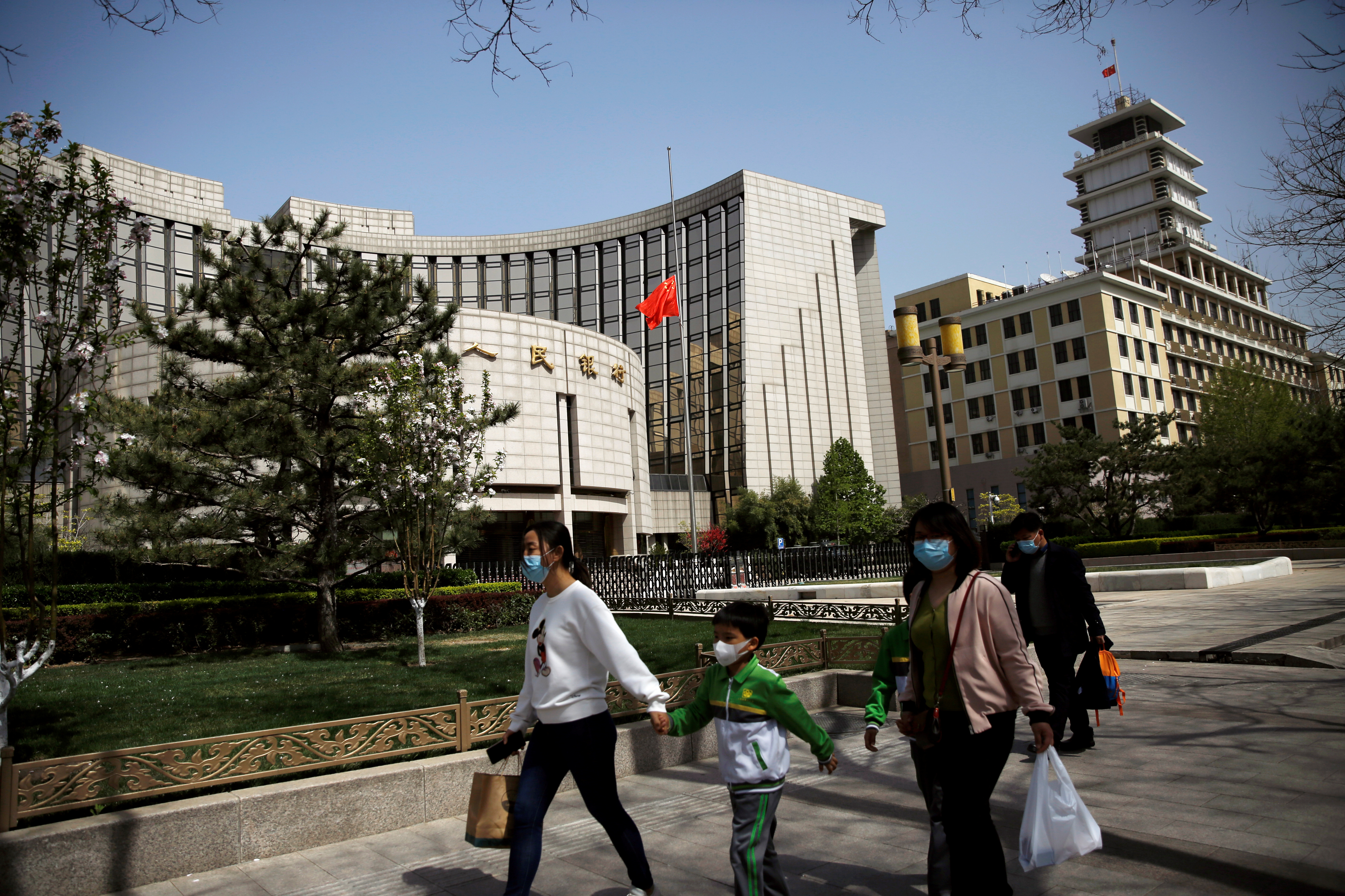 People wearing face masks walk past the headquarters of PBOC, where the Chinese national flag flies at half mast