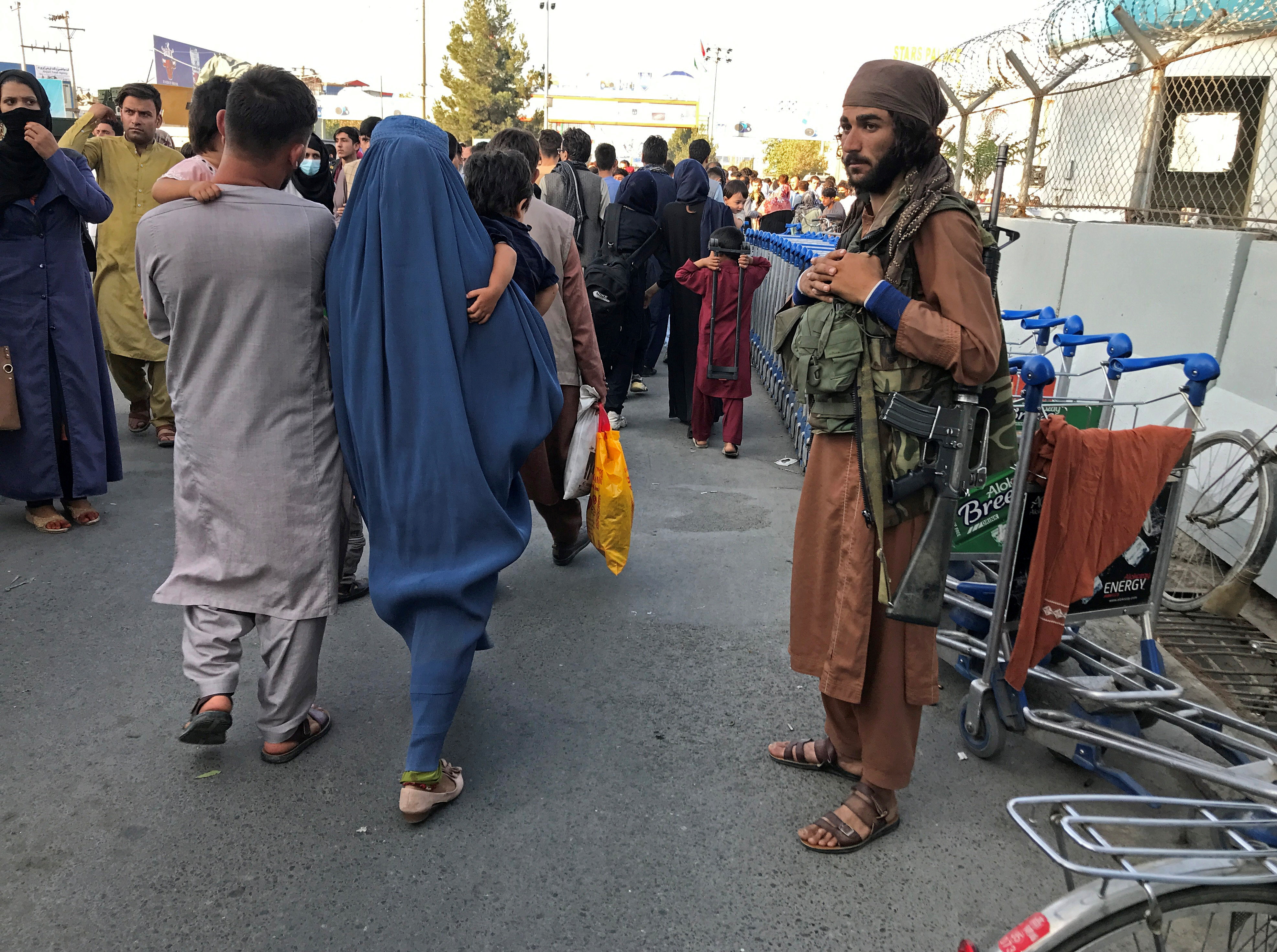 A member of Taliban stands guard as people walk at the entrance gate of Hamid Karzai International Airport in Kabul