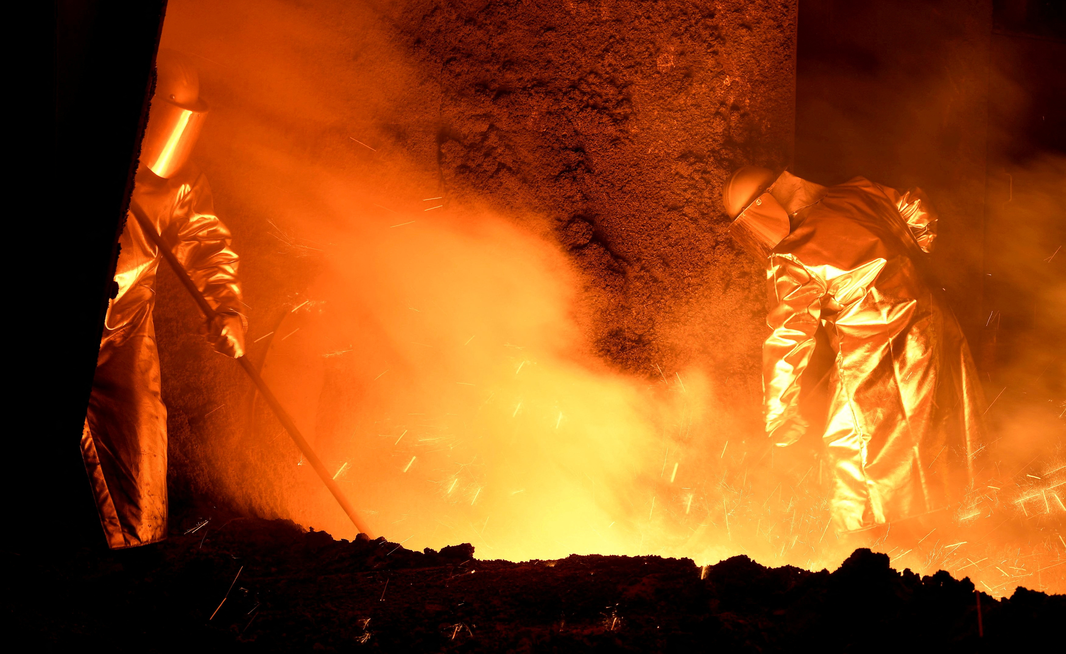 Steelworkers stand at a furnace at the plant of German steel company Salzgitter AG in Salzgitter