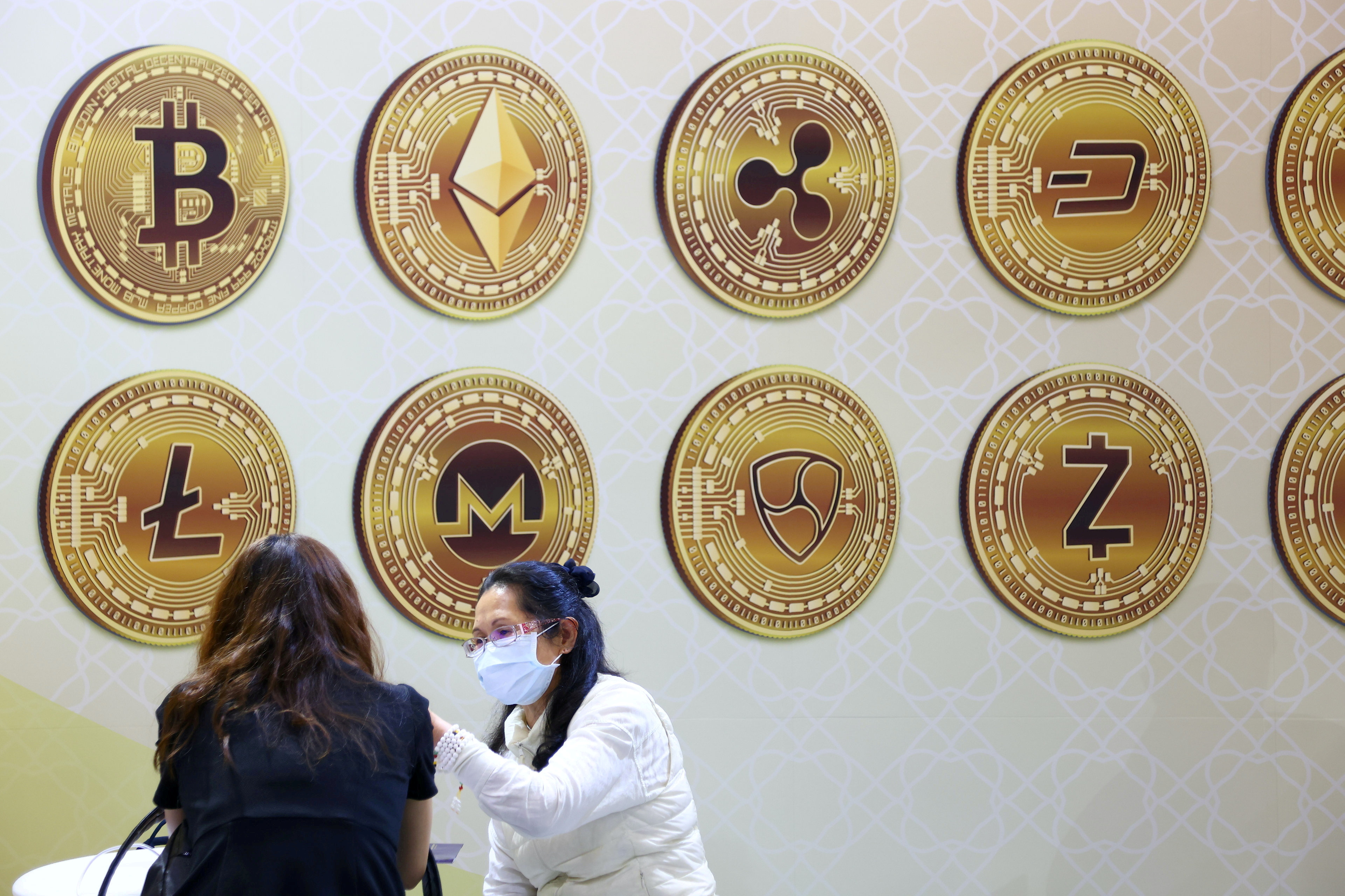 Customers talk against a backboard with signs of cryptocurrency during 2020 Taipei International Finance Expo in Taipei,