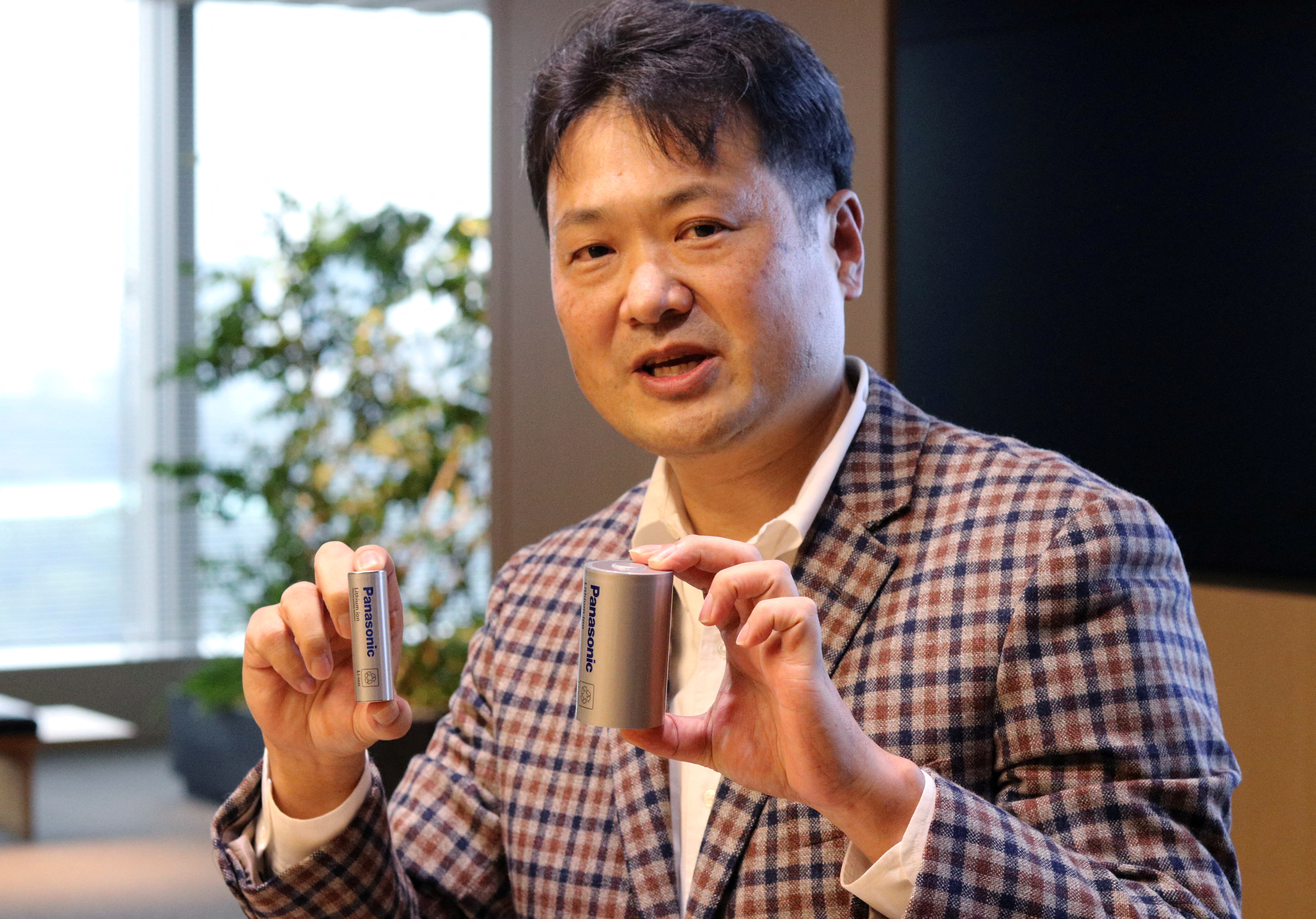 Kazuo Tadanobu, CEO of Panasonic's Energy Company, holds a prototype of the 4680 format battery cell (R) next to the current 2170 battery supplied to Tesla