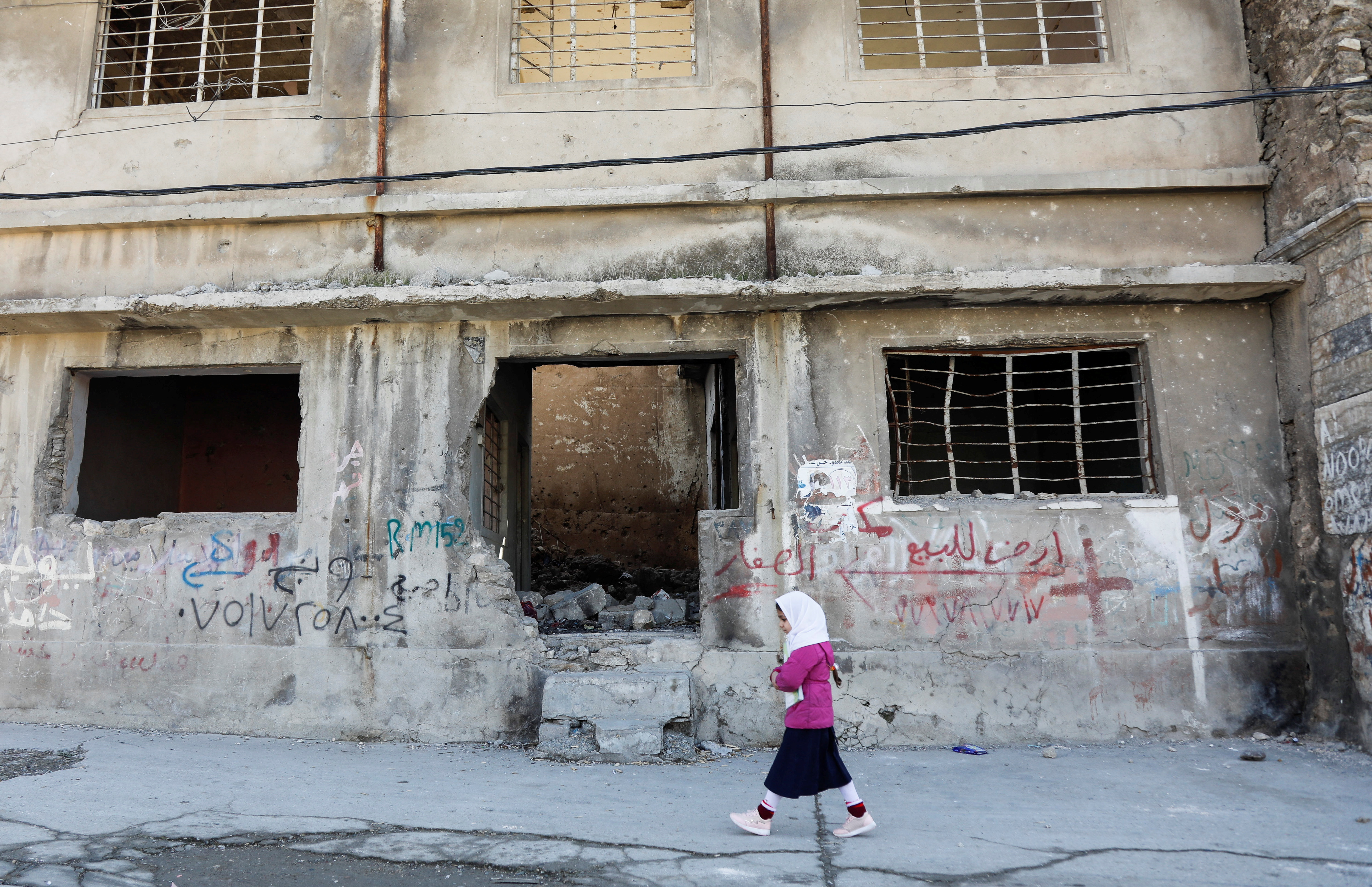 A girl walks near a building destroyed during past fighting with Islamic State militants