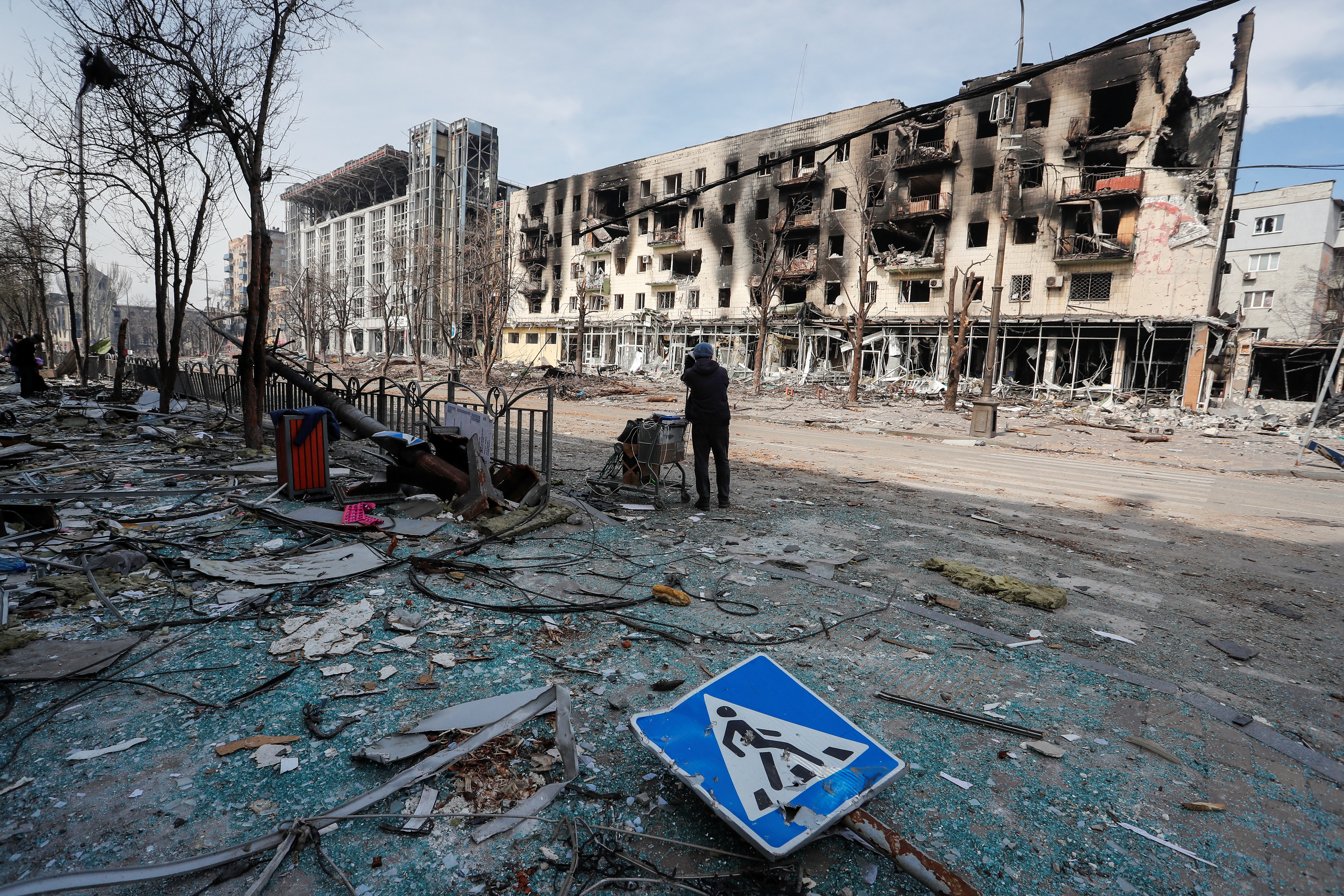 A resident stands with her belongings on a street near a building burnt in the course of the Ukraine-Russia conflict, in Mariupol