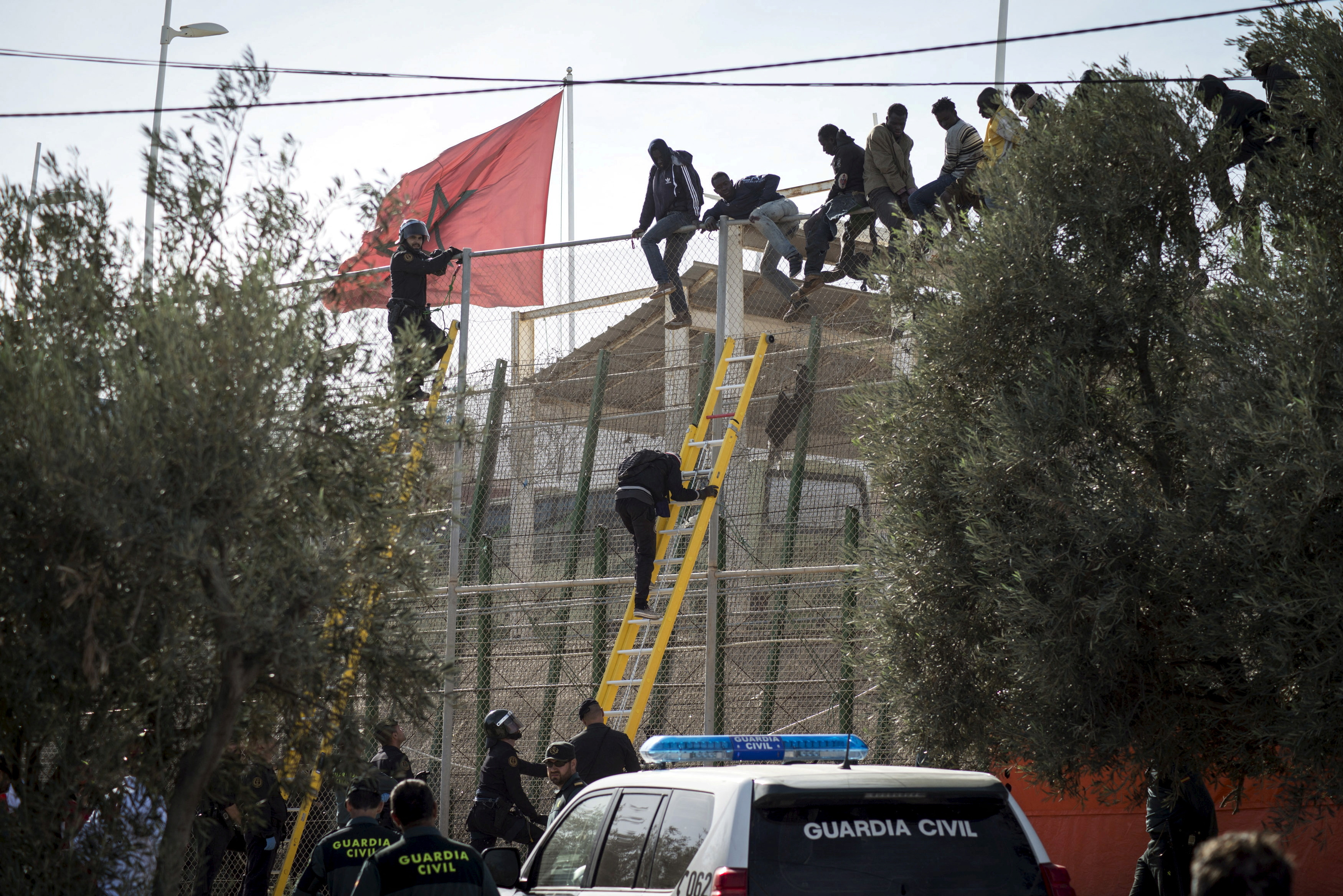 African migrants sit on top of a border fence during an attempt to cross into Spanish territories, between Morocco and Spain's north African enclave of Melilla