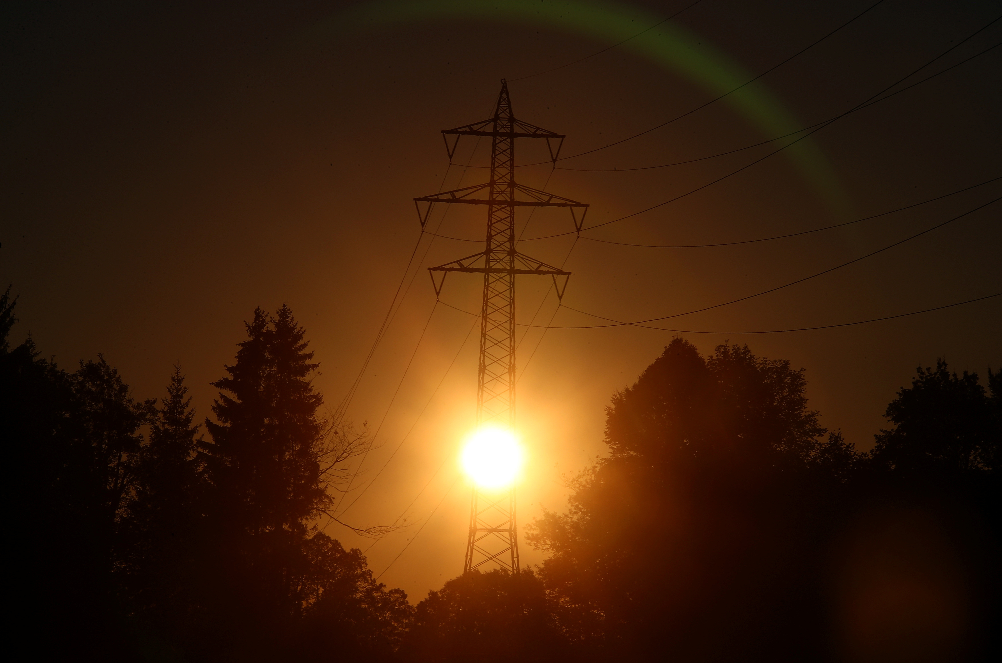 The sun rises behind high-voltage power lines and electricity pylons in Wall