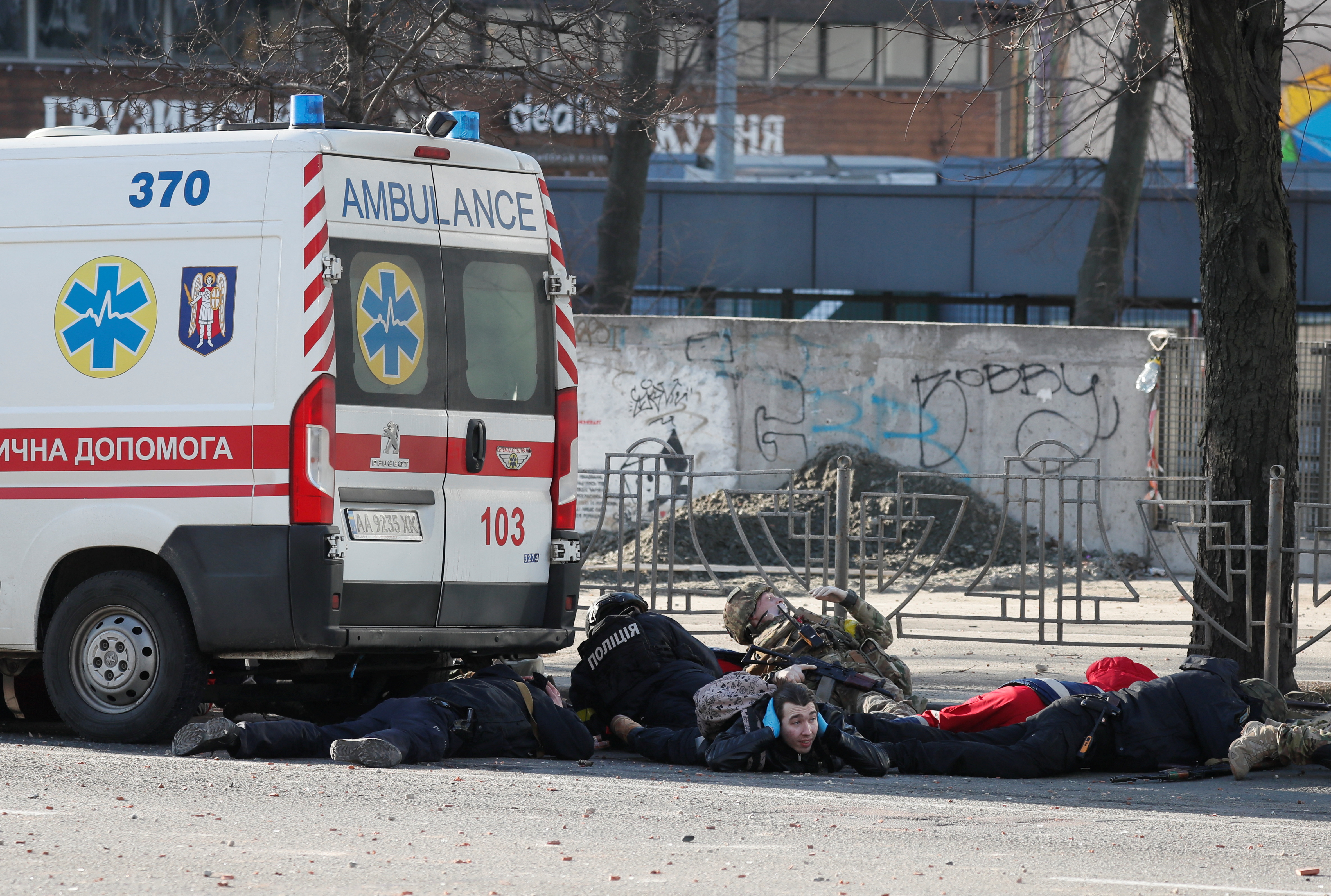 People take cover as an air-raid siren sounds, near an apartment building damaged by recent shelling in Kyiv, Ukraine February 26, 2022. REUTERS/Gleb Garanich