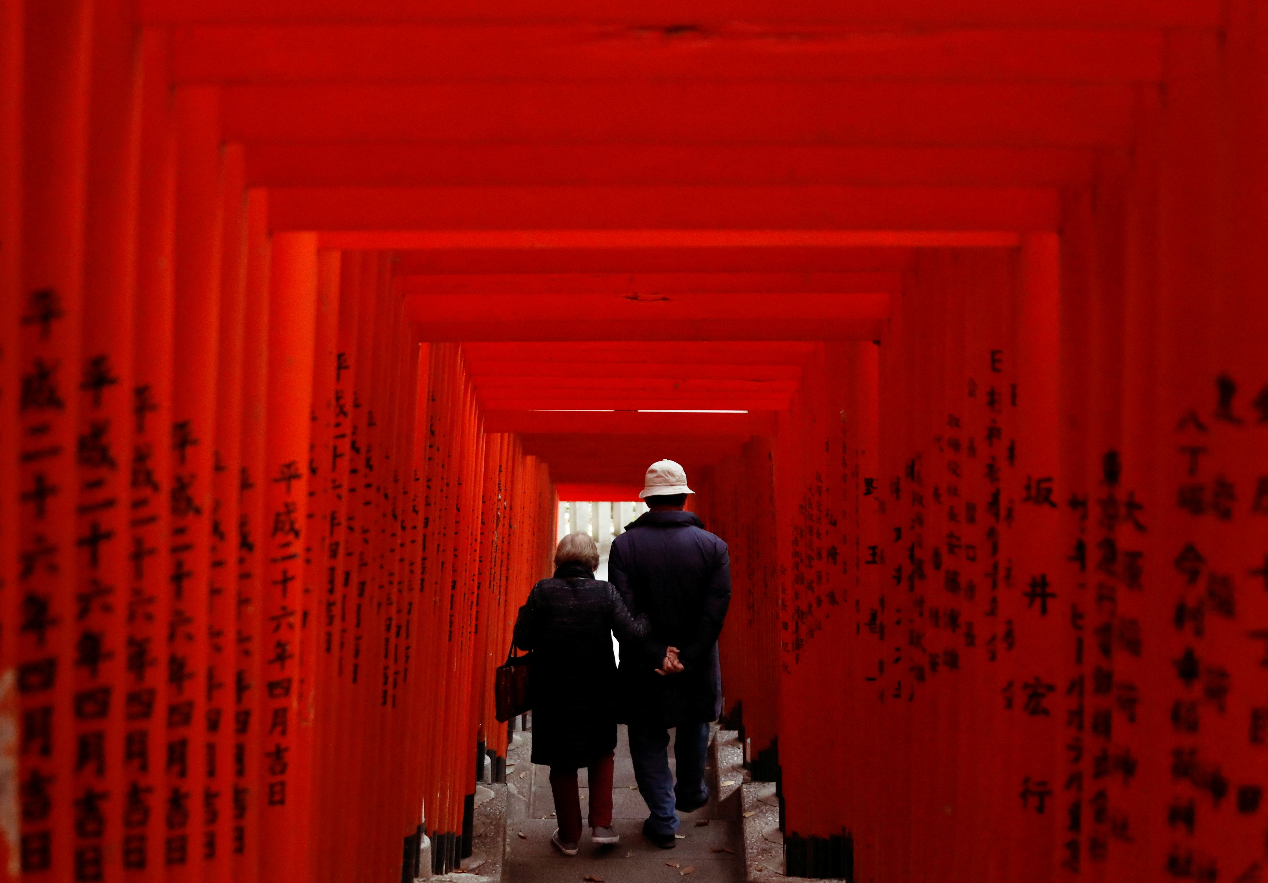 Sepasang lansia berjalan melewati gerbang torii kayu merah di sebuah kuil di Tokyo, di tengah wabah penyakit virus corona (COVID-19).