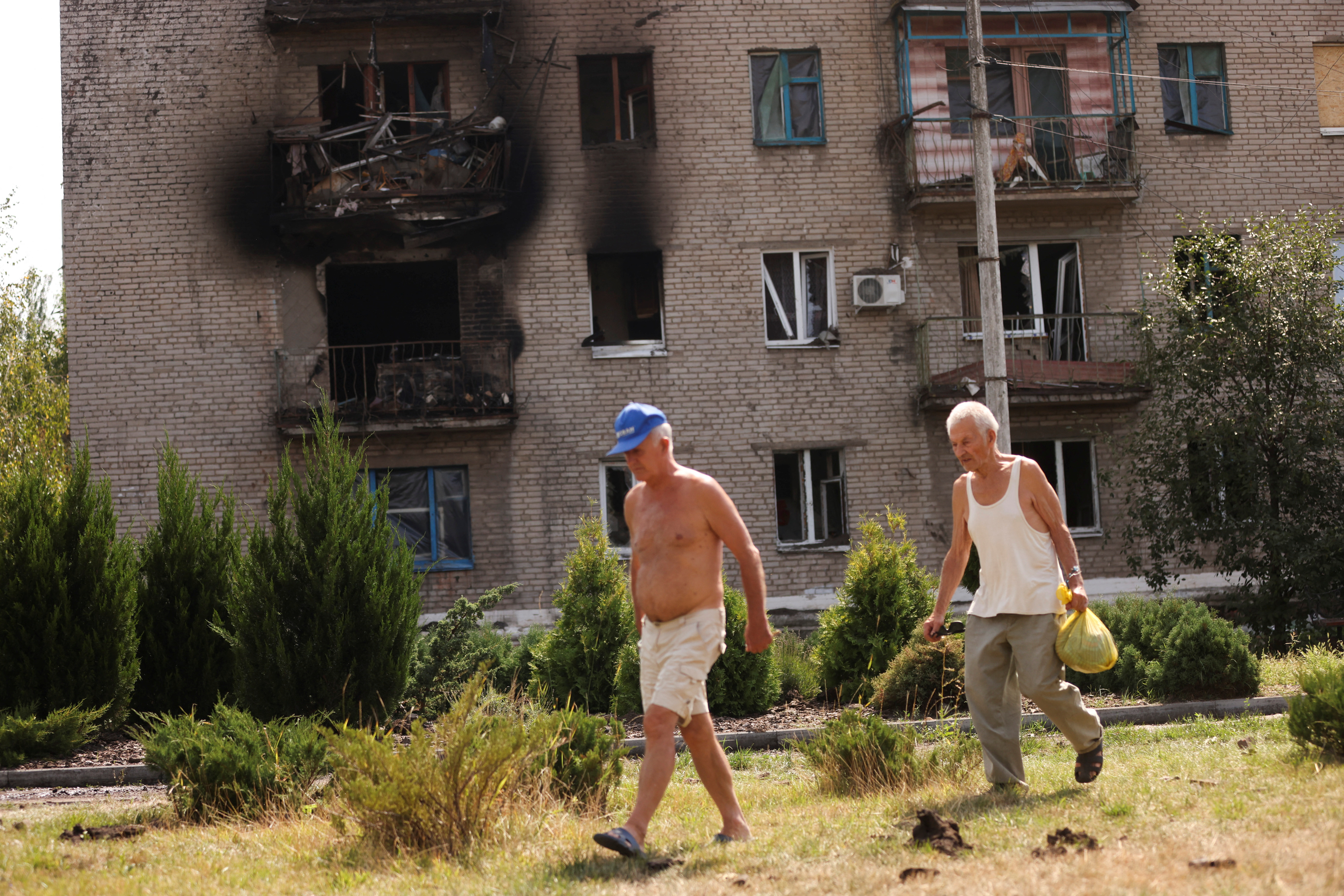 Ukrainian men walk in front of damaged houses following recent Russian shelling in the city of Slovyansk