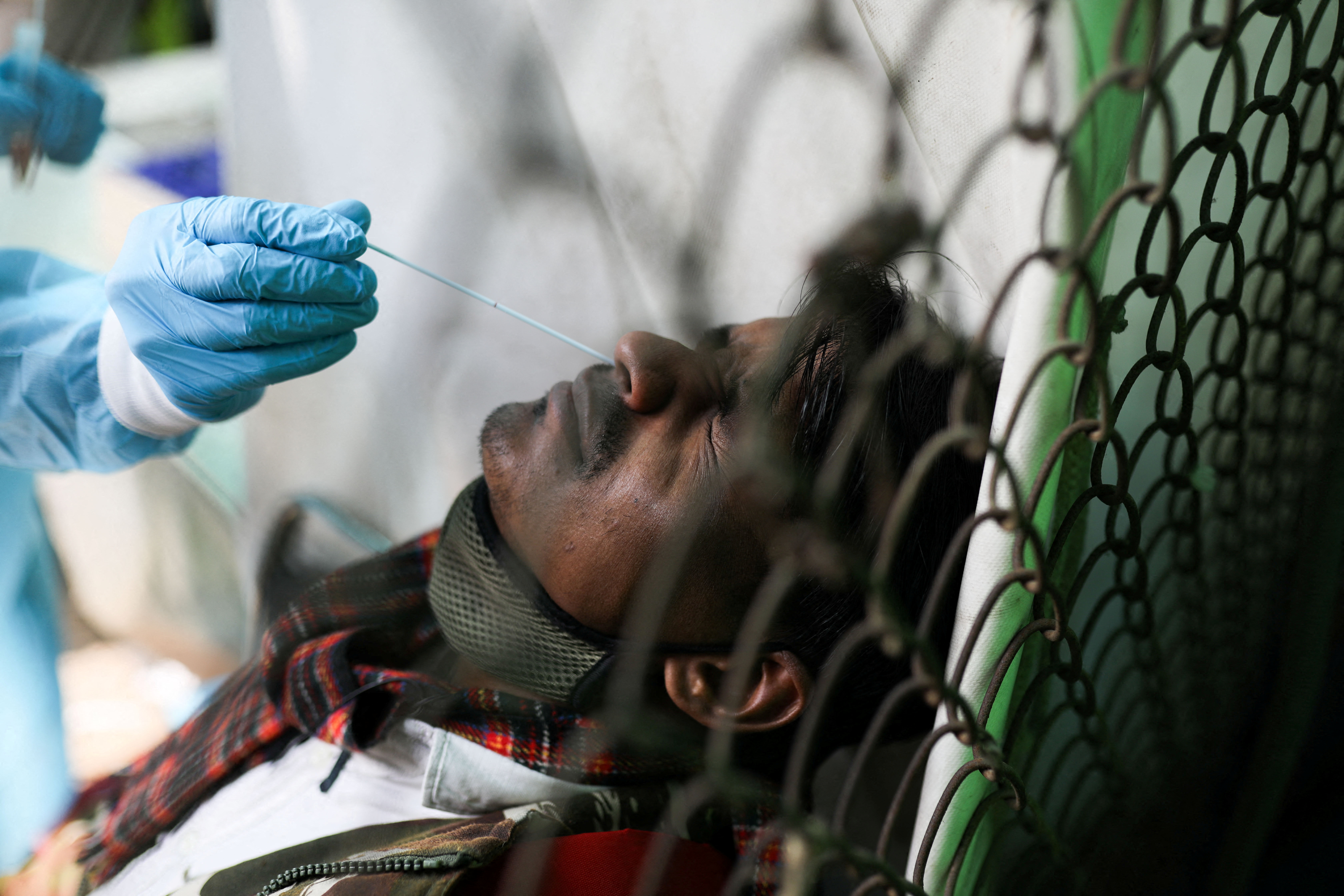 A healthcare worker collects a COVID-19 test swab sample from a man in New Delhi