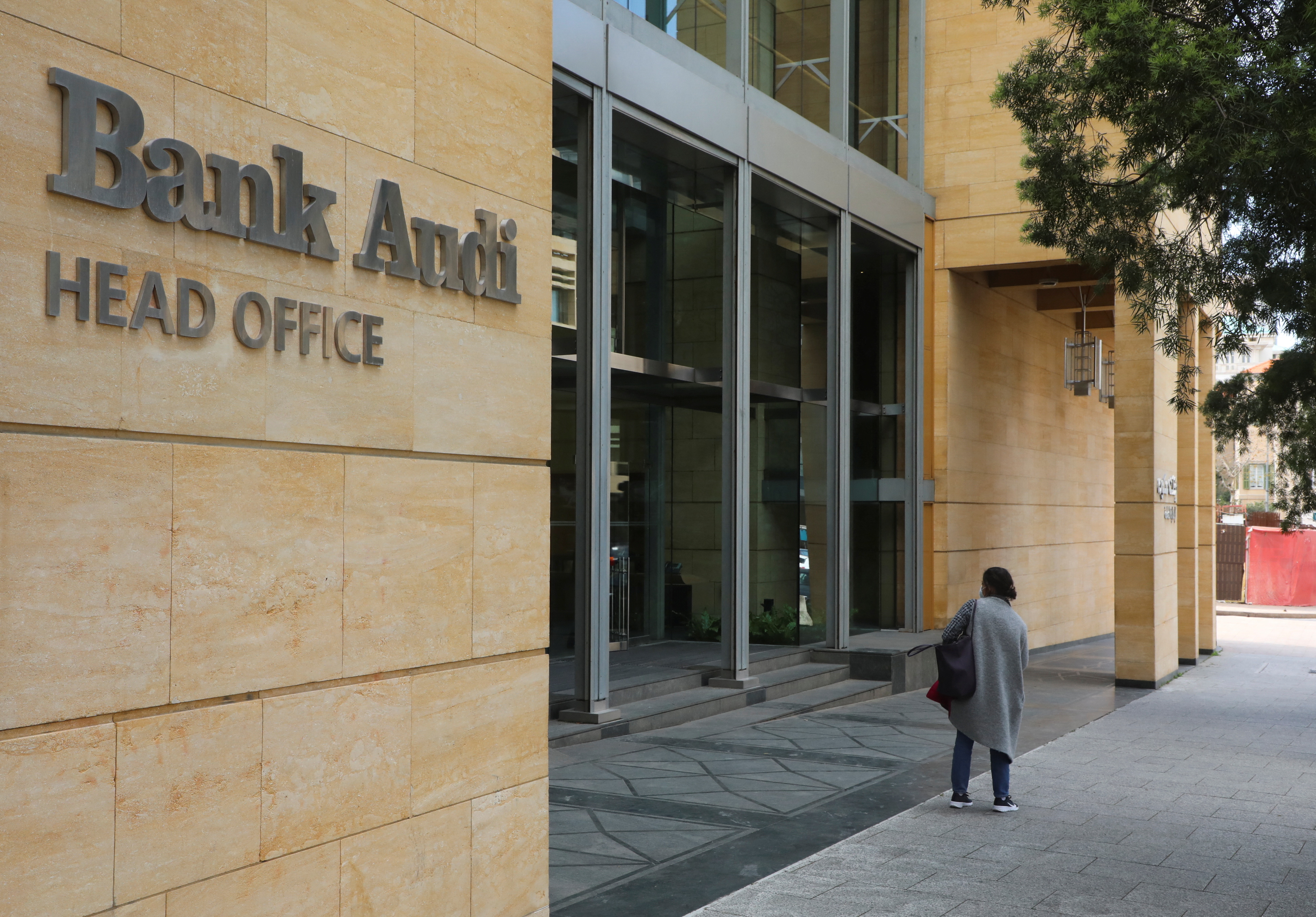 A woman stands near a logo of Bank Audi, as seen at the entrance of the Bank's head office in Beirut