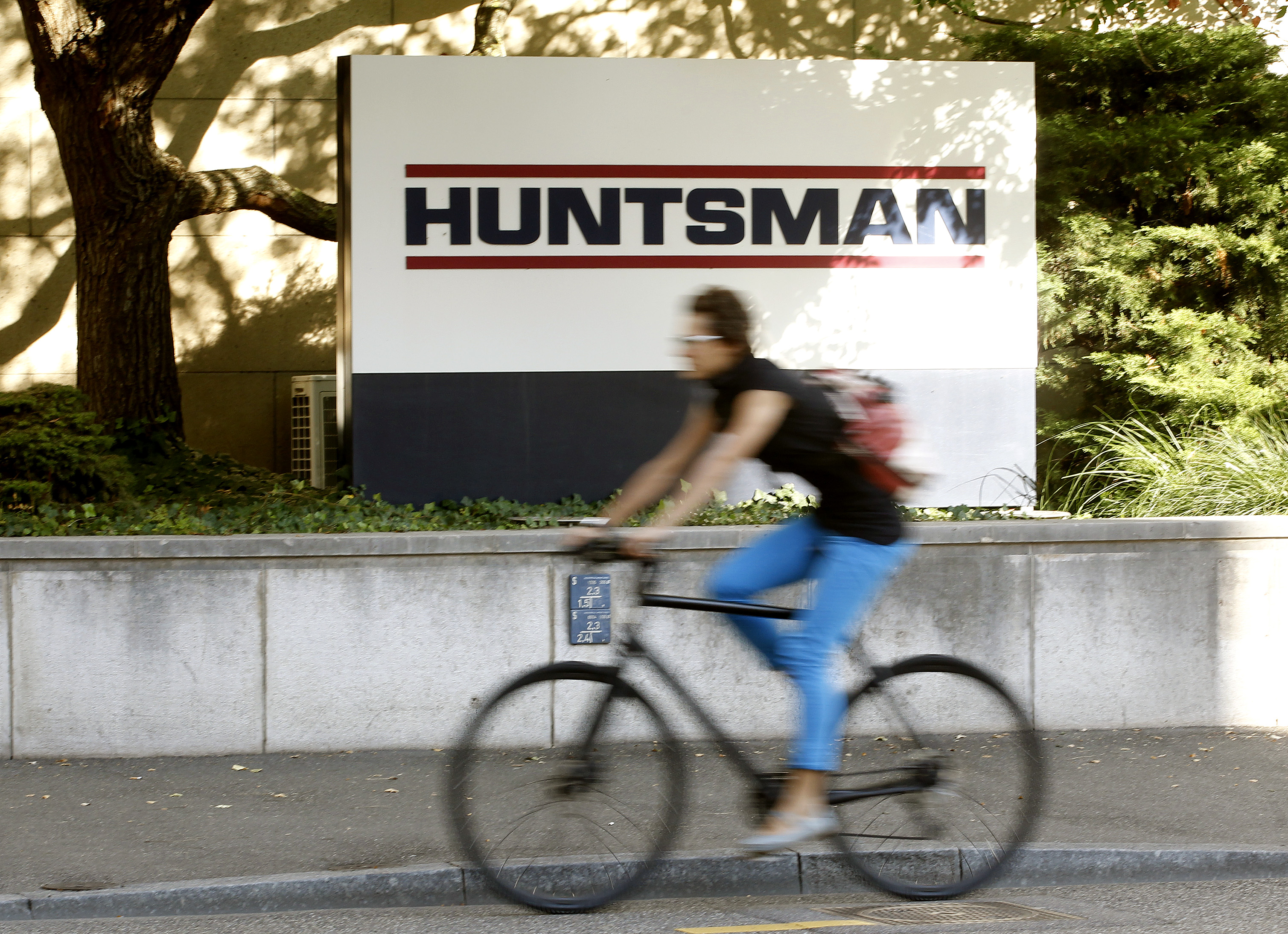 A woman cycles past the logo of U.S. chemical company Huntsman in front of a plant in Basel