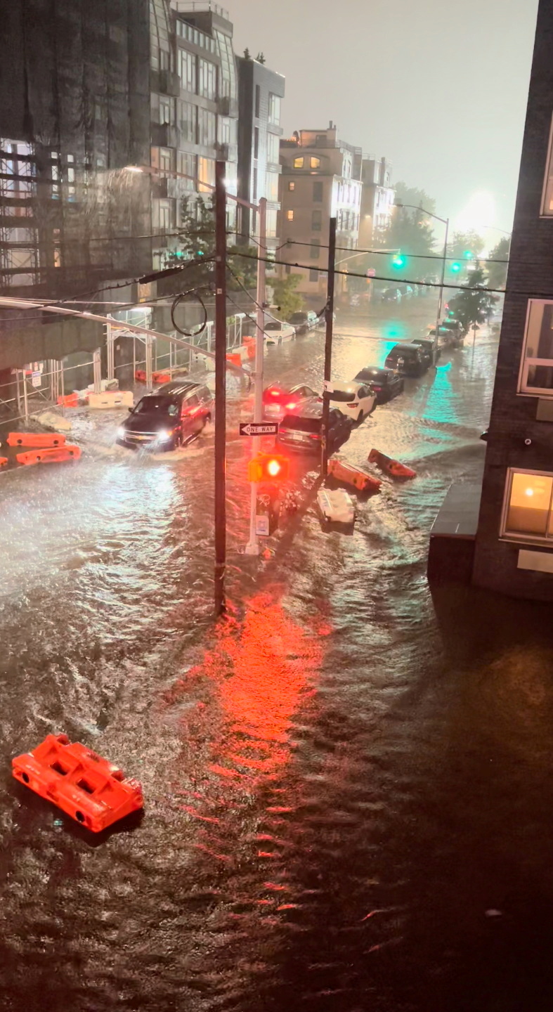A vehicle moves along a flooded road as safety barriers float in floodwaters in Williamsburg, in the Brooklyn borough of New York City, New York, U.S. September 1, 2021, in this still image taken from video obtained from social media. Mandatory credit JAYMEE SIRE/via REUTERS 