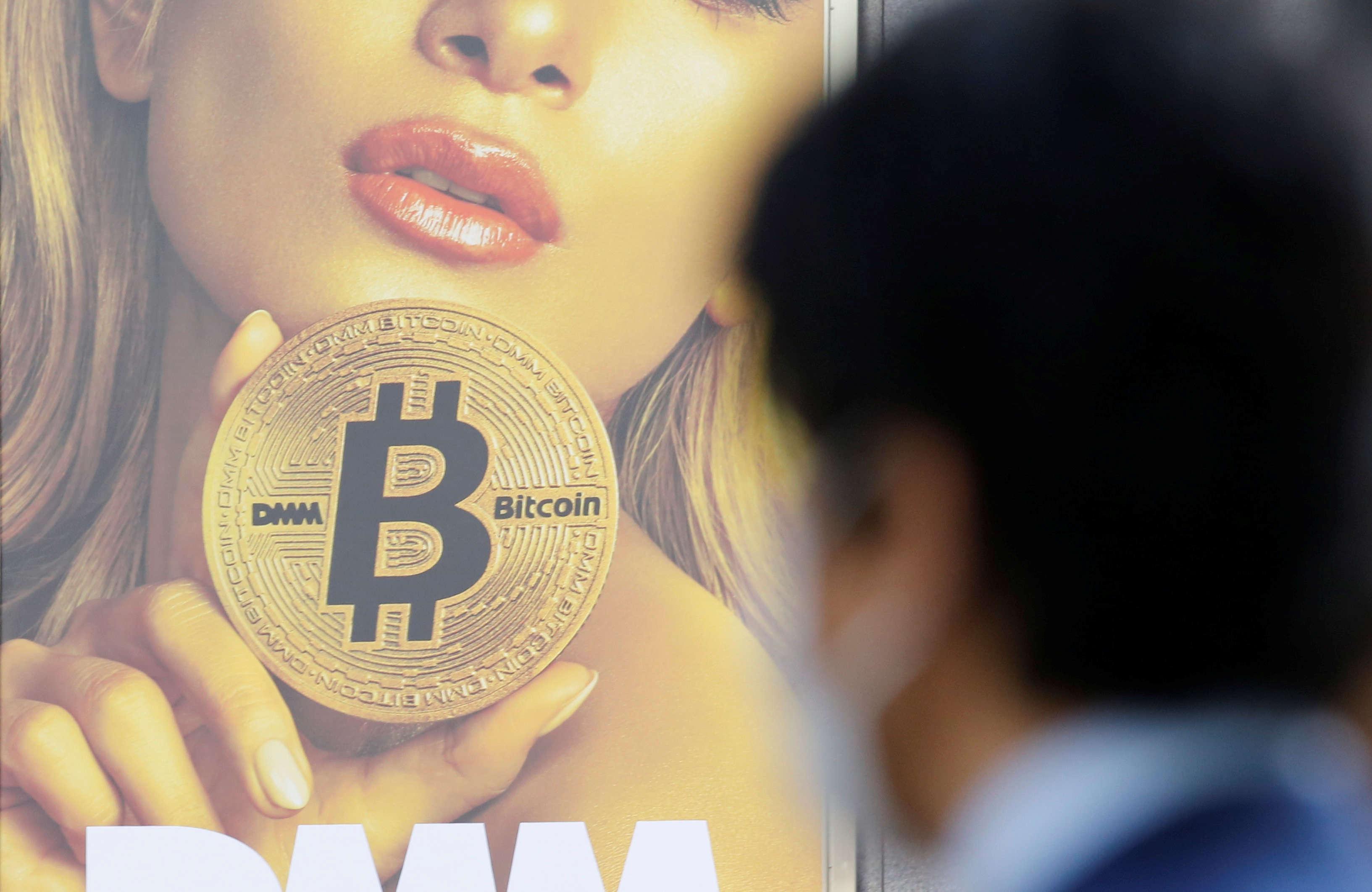 A man stands near an advertisement of a cryptocurrency exchange in Tokyo