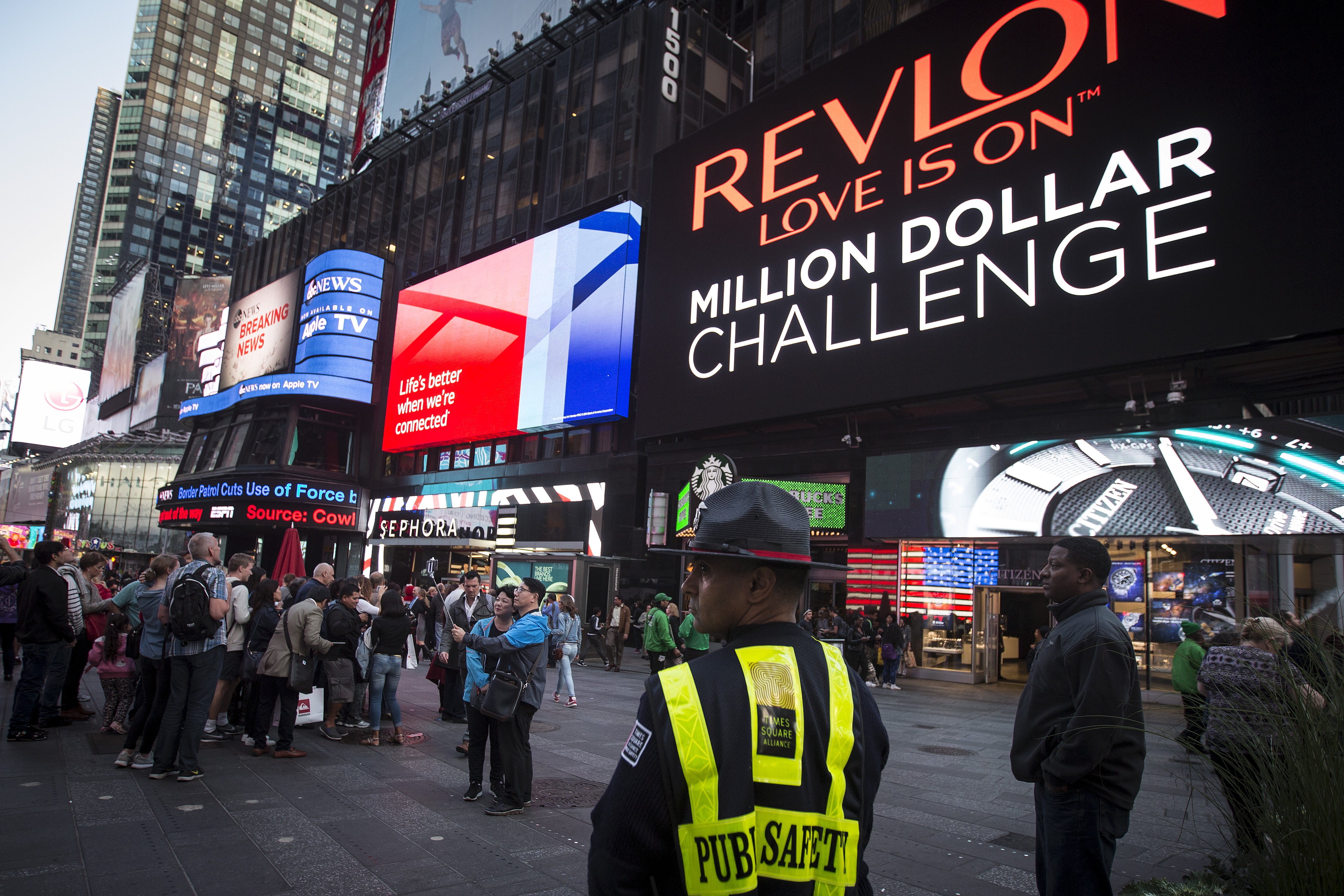 A Public Safety officer keeps watch as people stand in front of  a billboard owned by Revlon that takes their pictures and displays them in Times Square in the Manhattan borough of New York