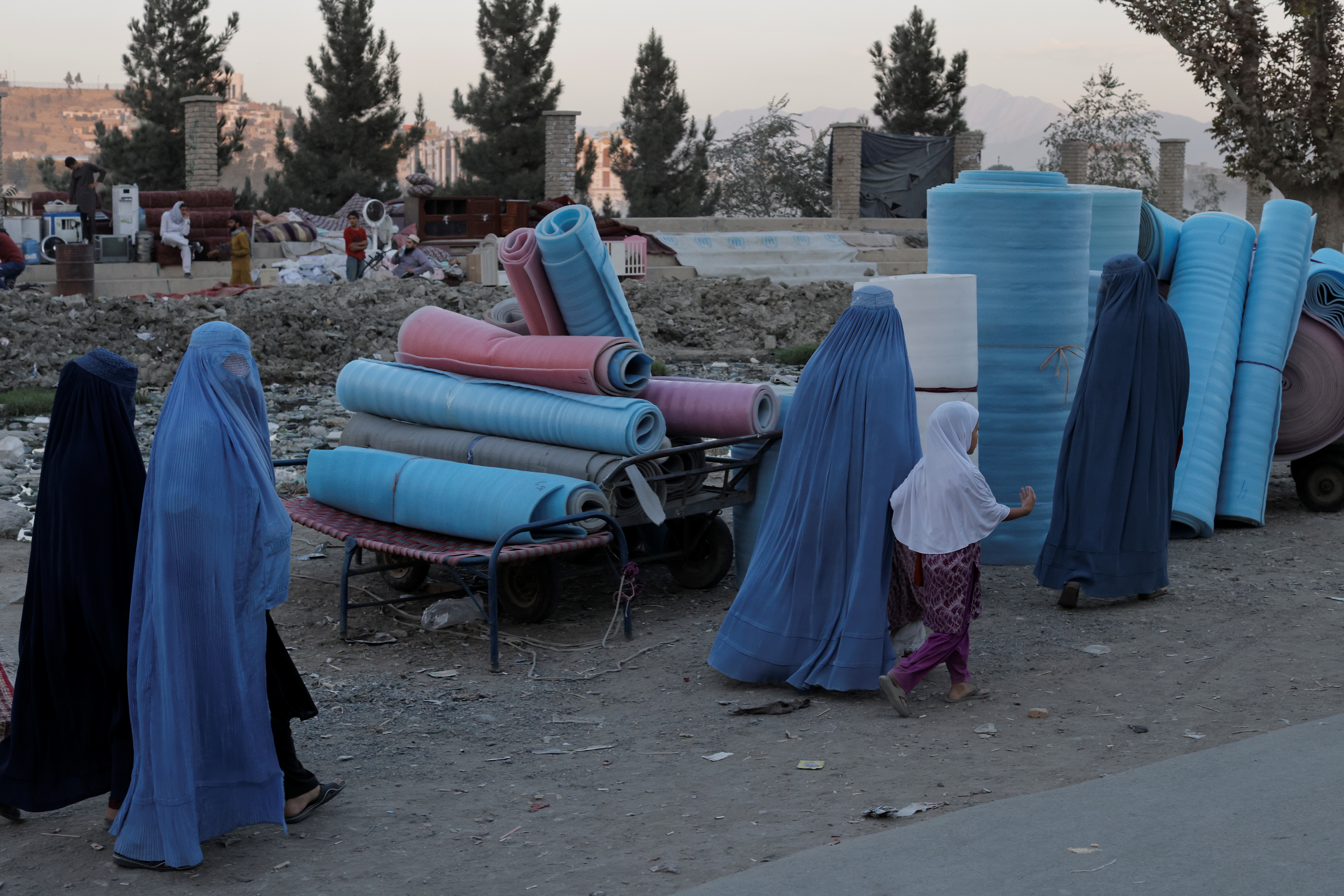 Women wearing burqas walk in a second-hand market where people sell their home appliances and other belongings in Kabul
