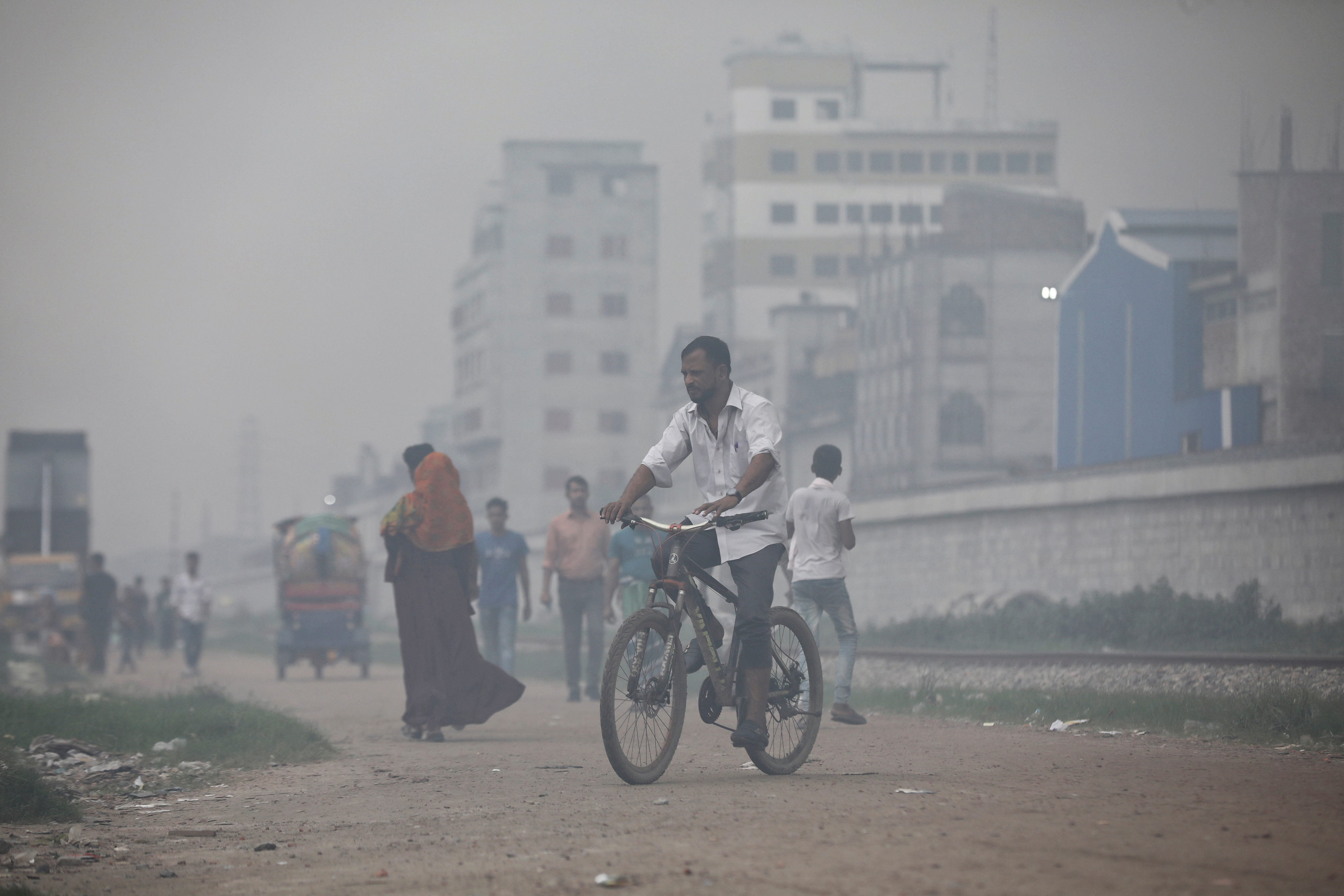 A man rides a bicycle through smoke rising from steel mills located near a slum in Dhaka