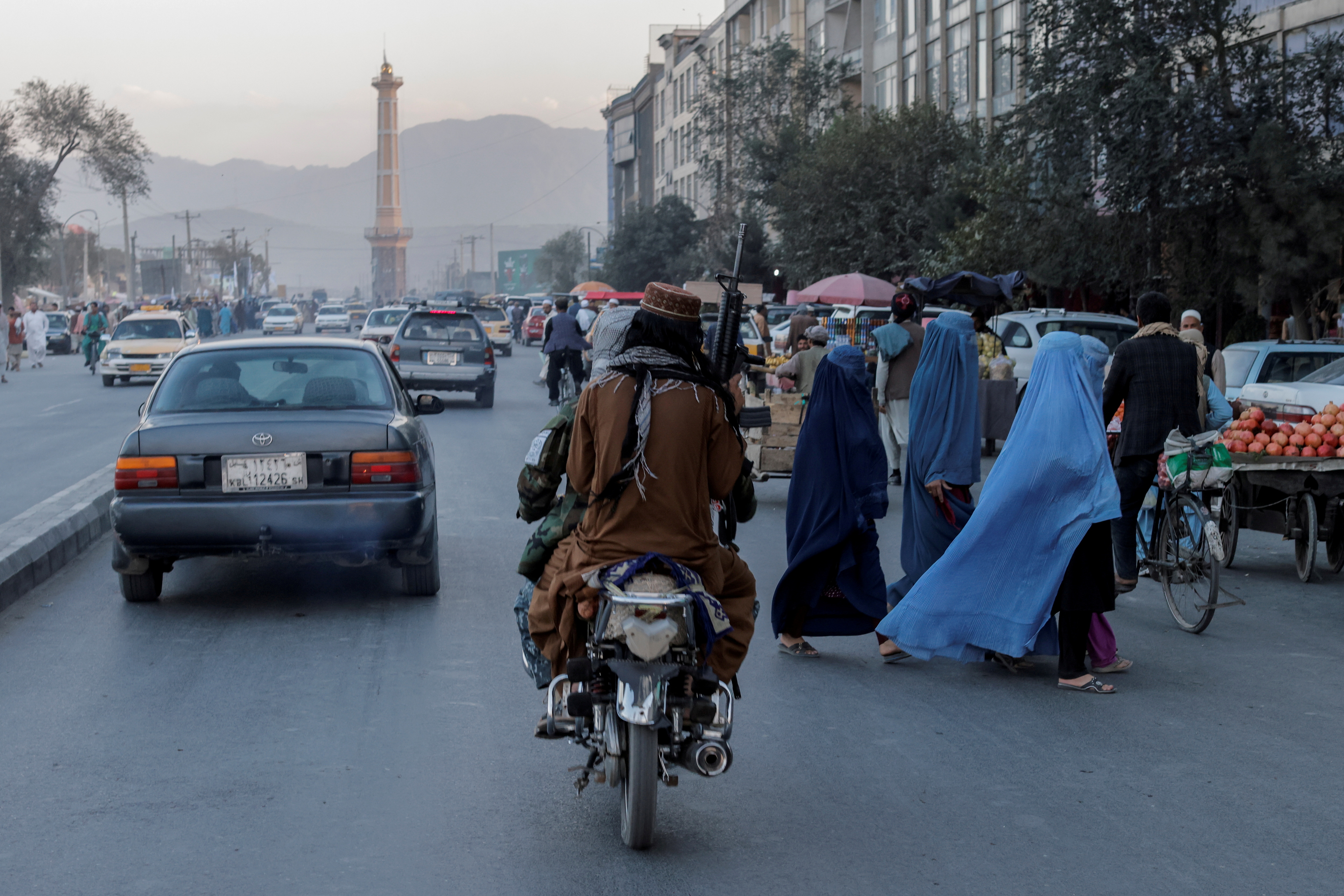 A group of women wearing burqas crosses the street as members of the Taliban drive past in Kabul, Afghanistan October 9, 2021. REUTERS/Jorge Silva/File Photo