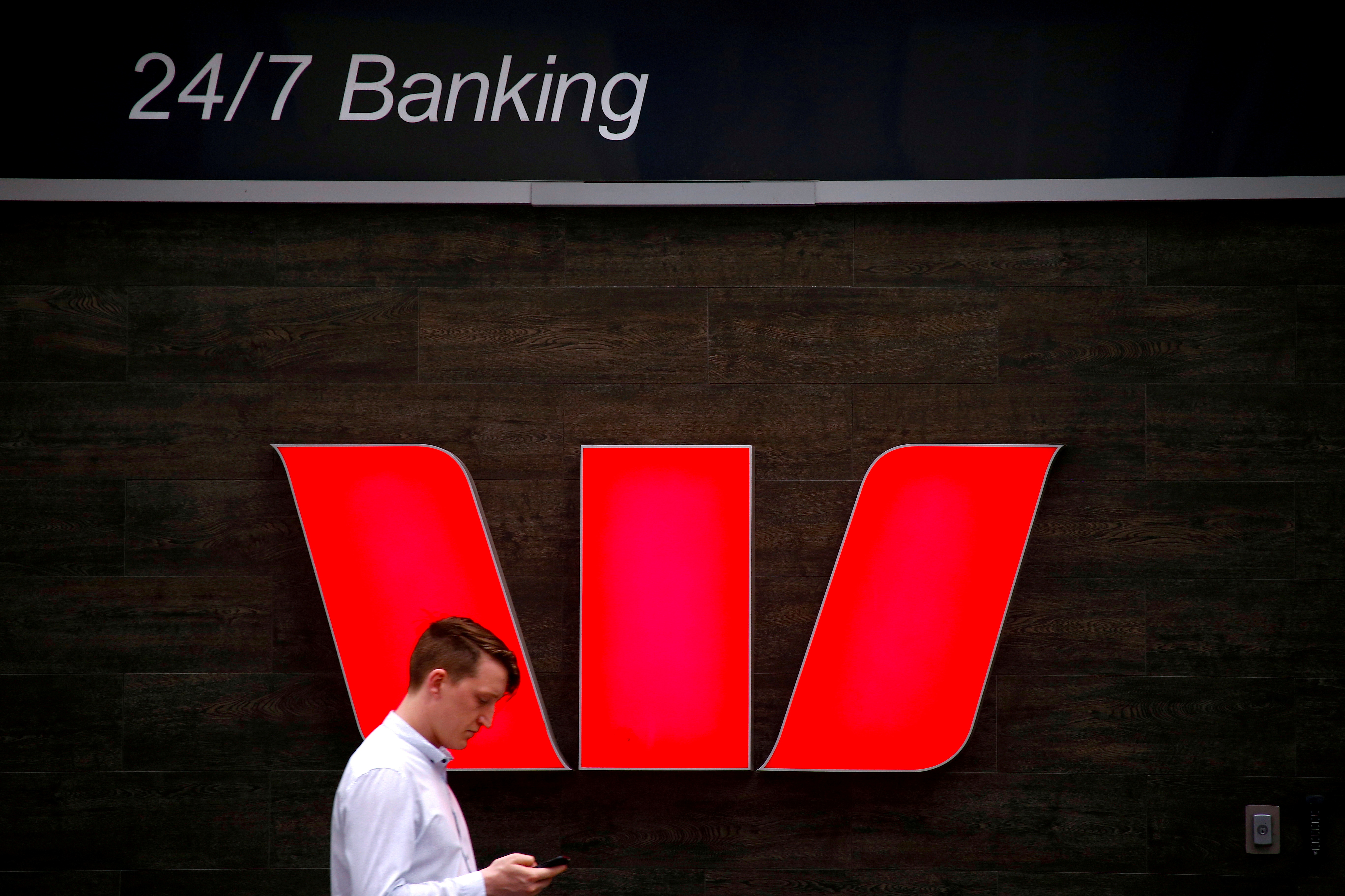 A pedestrian looks at his phone as he walks past a logo for Australia's Westpac Banking Corp located outside a branch in central Sydney