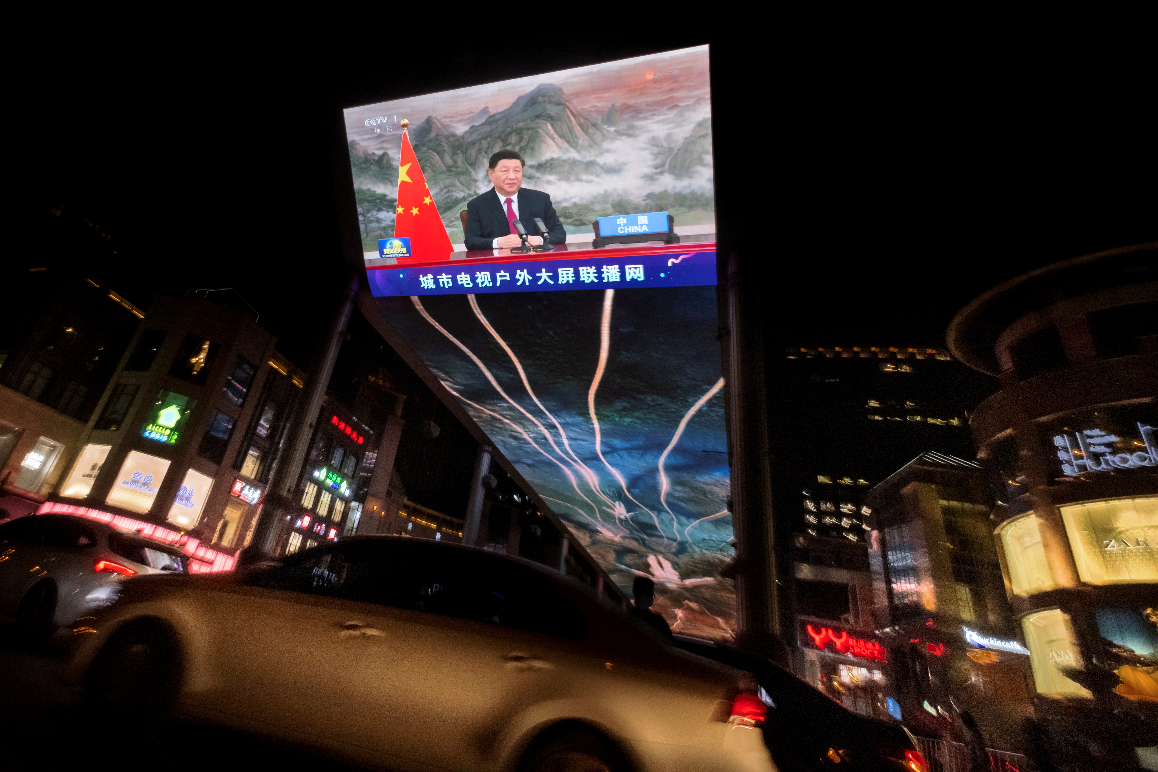 A screen displays a CCTV state media news broadcast showing Chinese President Xi Jinping addressing world leaders at the G20 meeting in Rome via video link at a shopping mall in Beijing