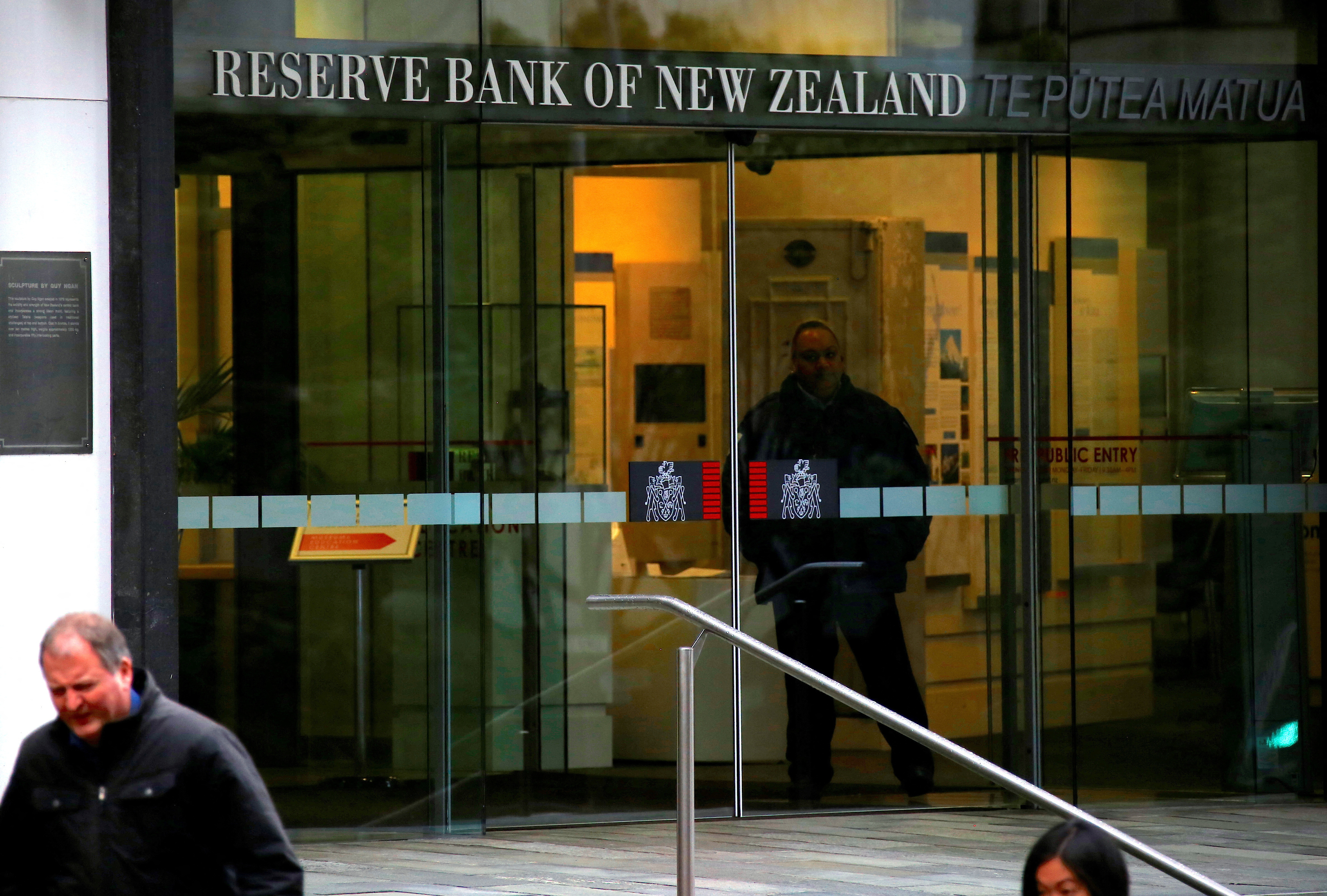 Pedestrians walk past as a security guard stands in the main entrance to the Reserve Bank of New Zealand located in central Wellington, New Zealand
