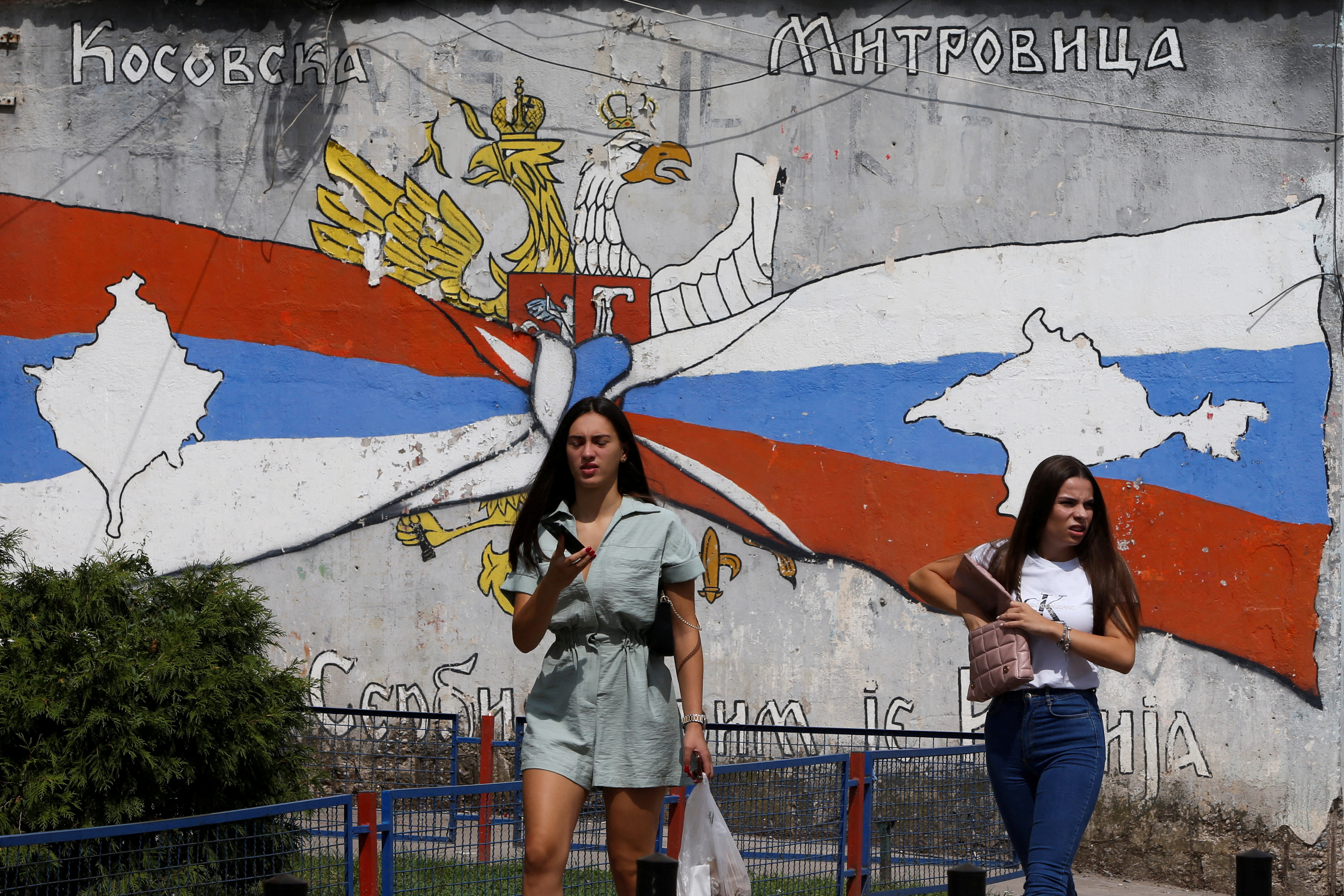 Women walk past a mural in North Mitrovica
