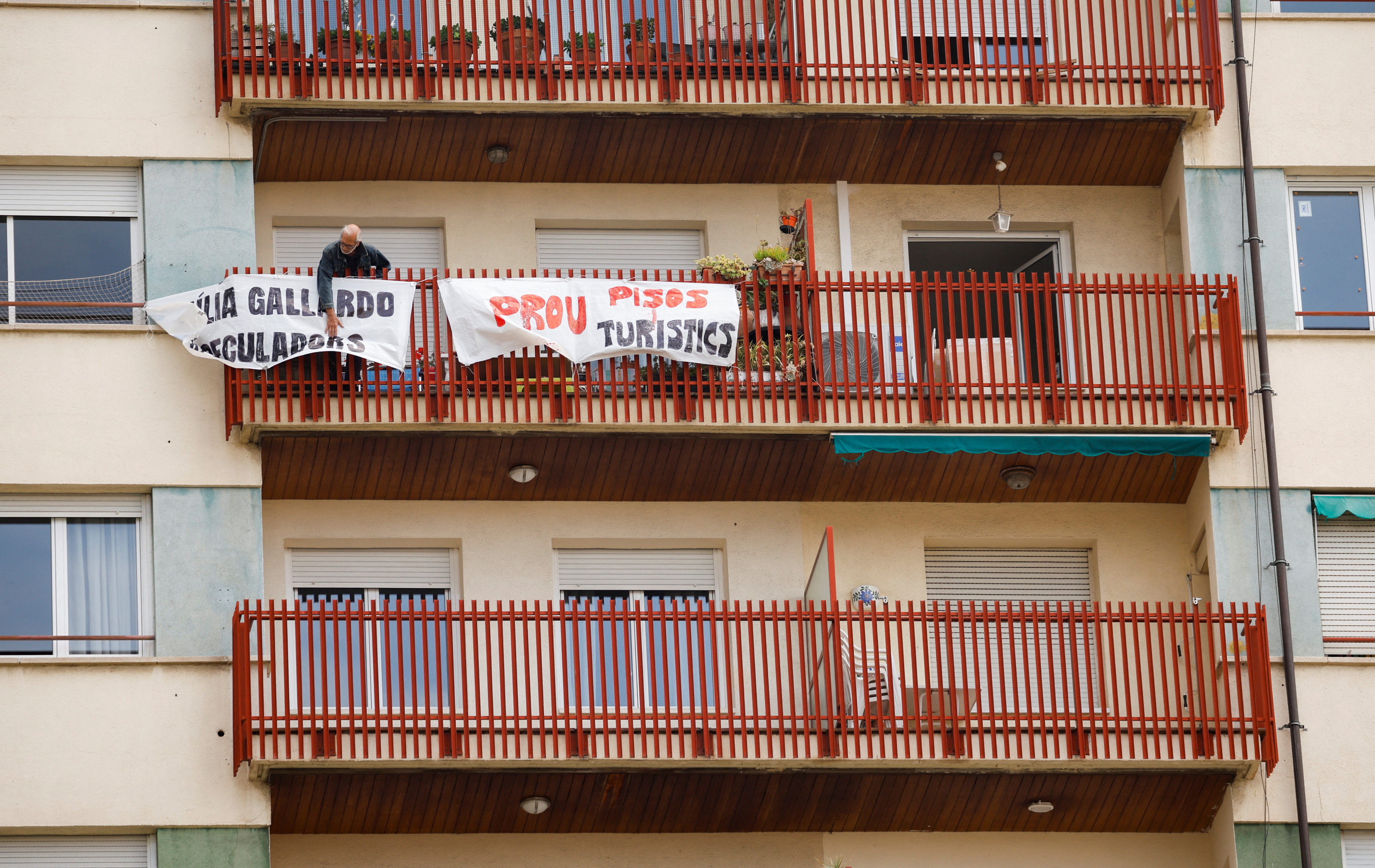 A man ties protest banners in the balcony of a building that was recently converted for tourist use at Sants neighborhood in Barcelona