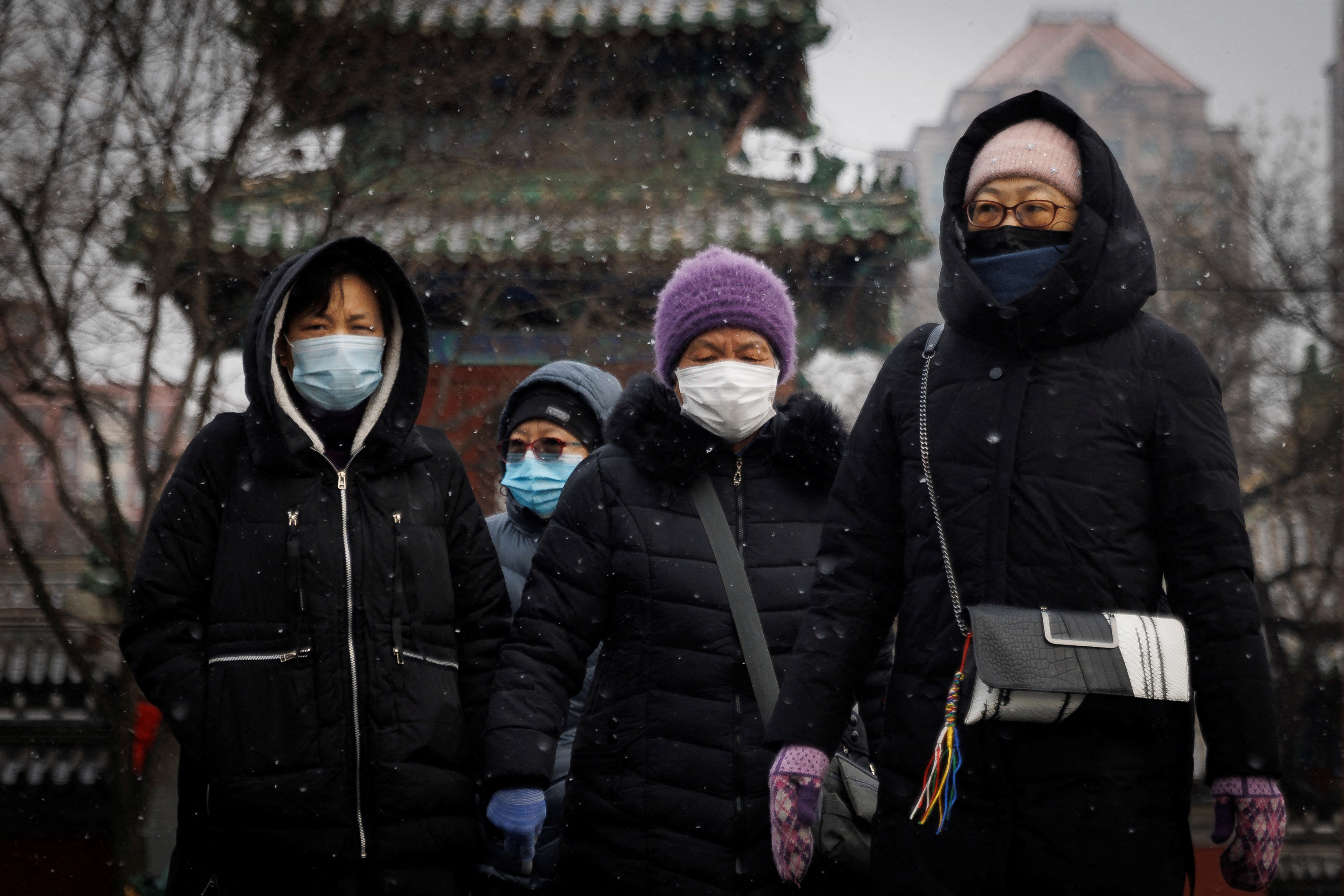 People wear face masks as they walk on a snowy morning as the coronavirus disease (COVID-19) continues in Beijing