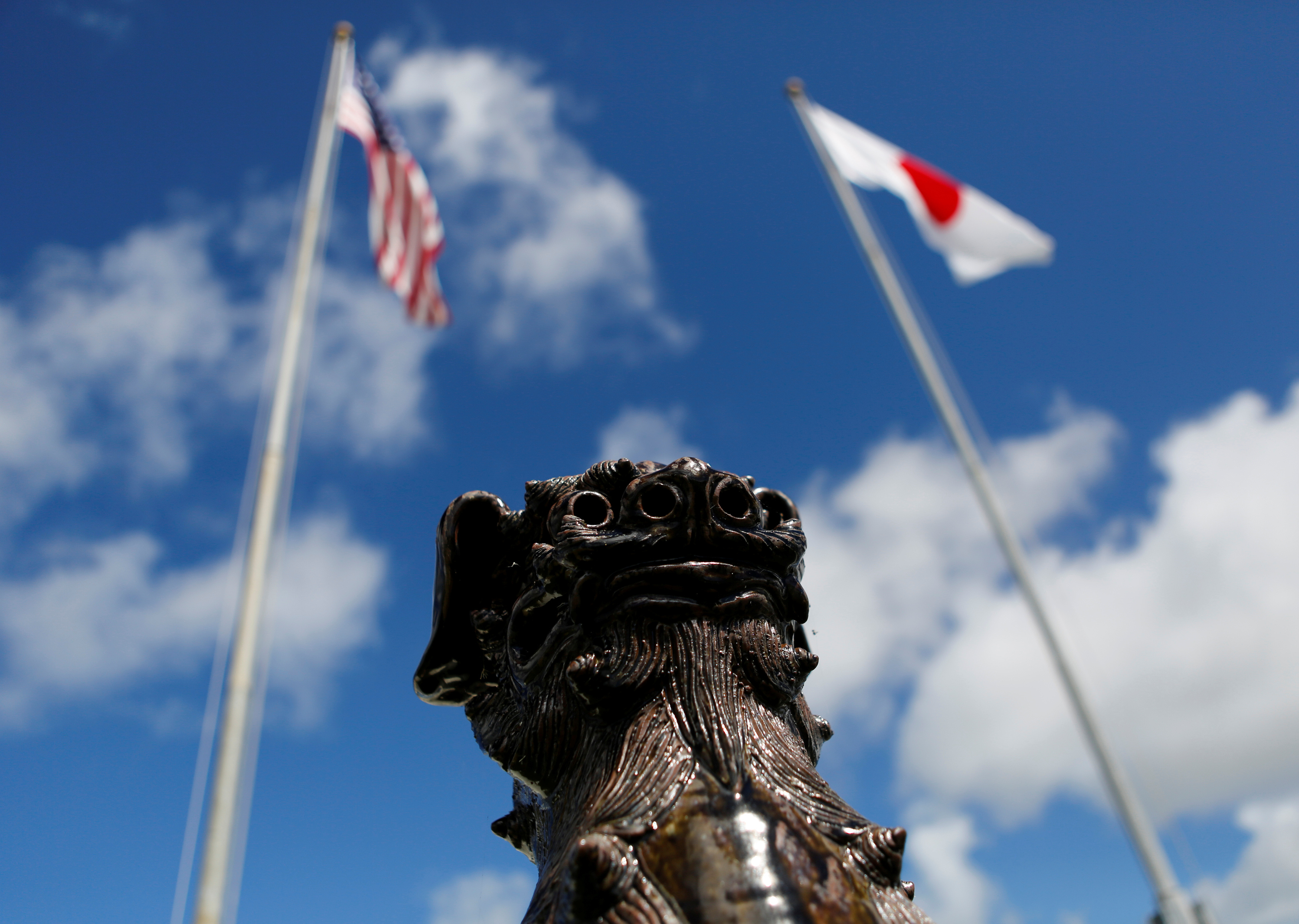 The U.S. and Japanese national flags are hoisted next to a traditional Okinawan Shisa statue at the U.S. Marine's Camp Foster in Ginowan