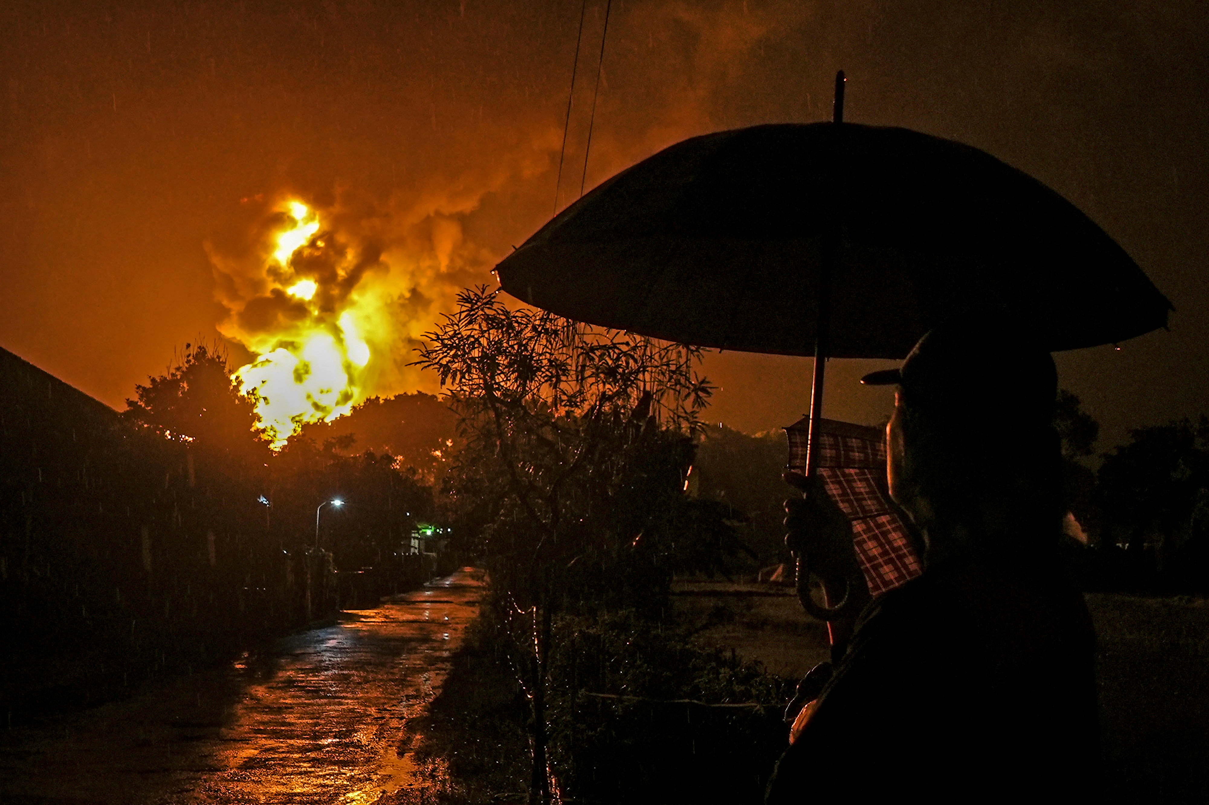 A man carrying an umbrella looks at fire at a fuel storage unit at the Pertamina refinery complex in Cilacap