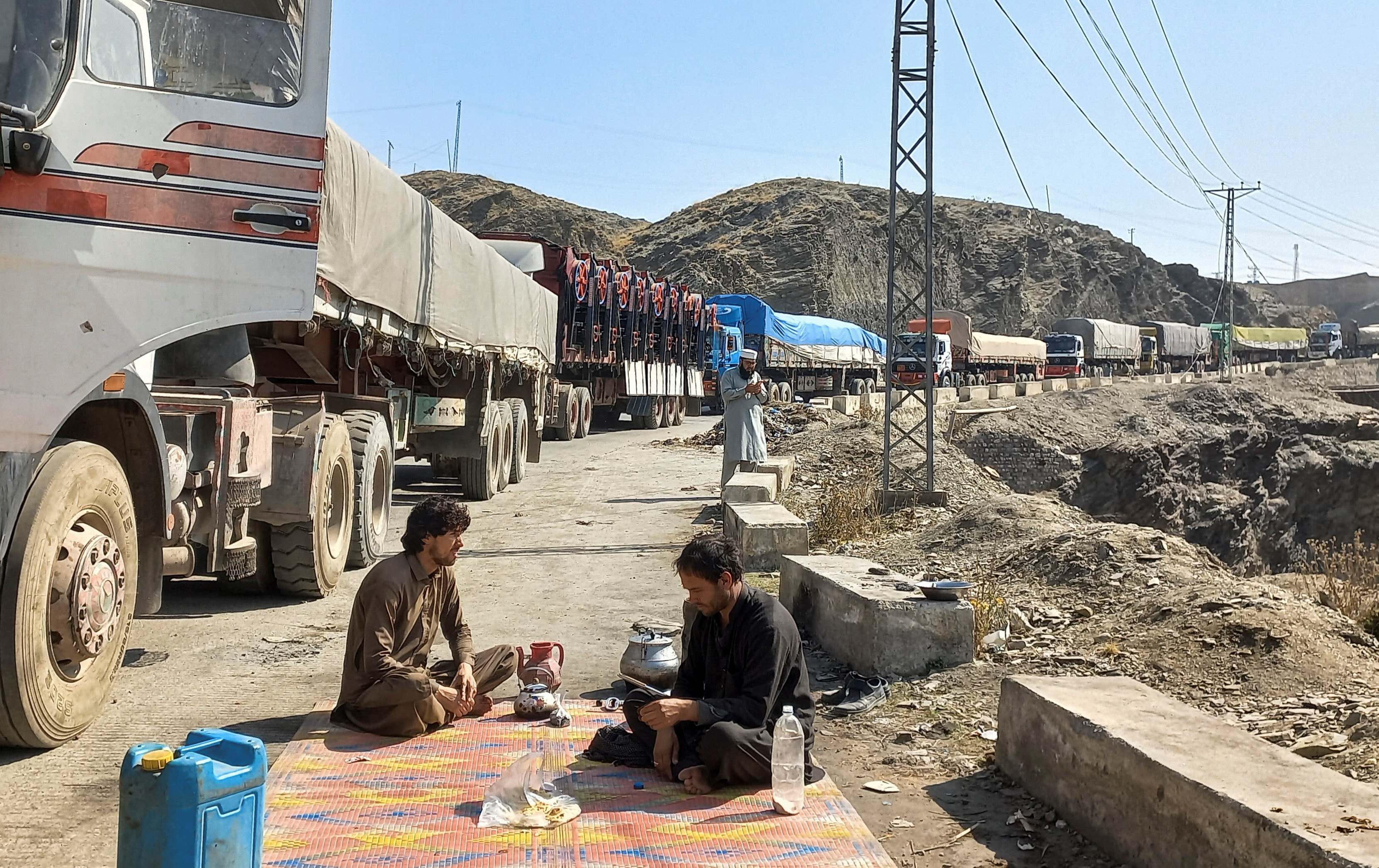 Men sit near a queue of trucks loaded with supplies to leave for Afghanistan, after Taliban authorities have closed the main border crossing in Torkham