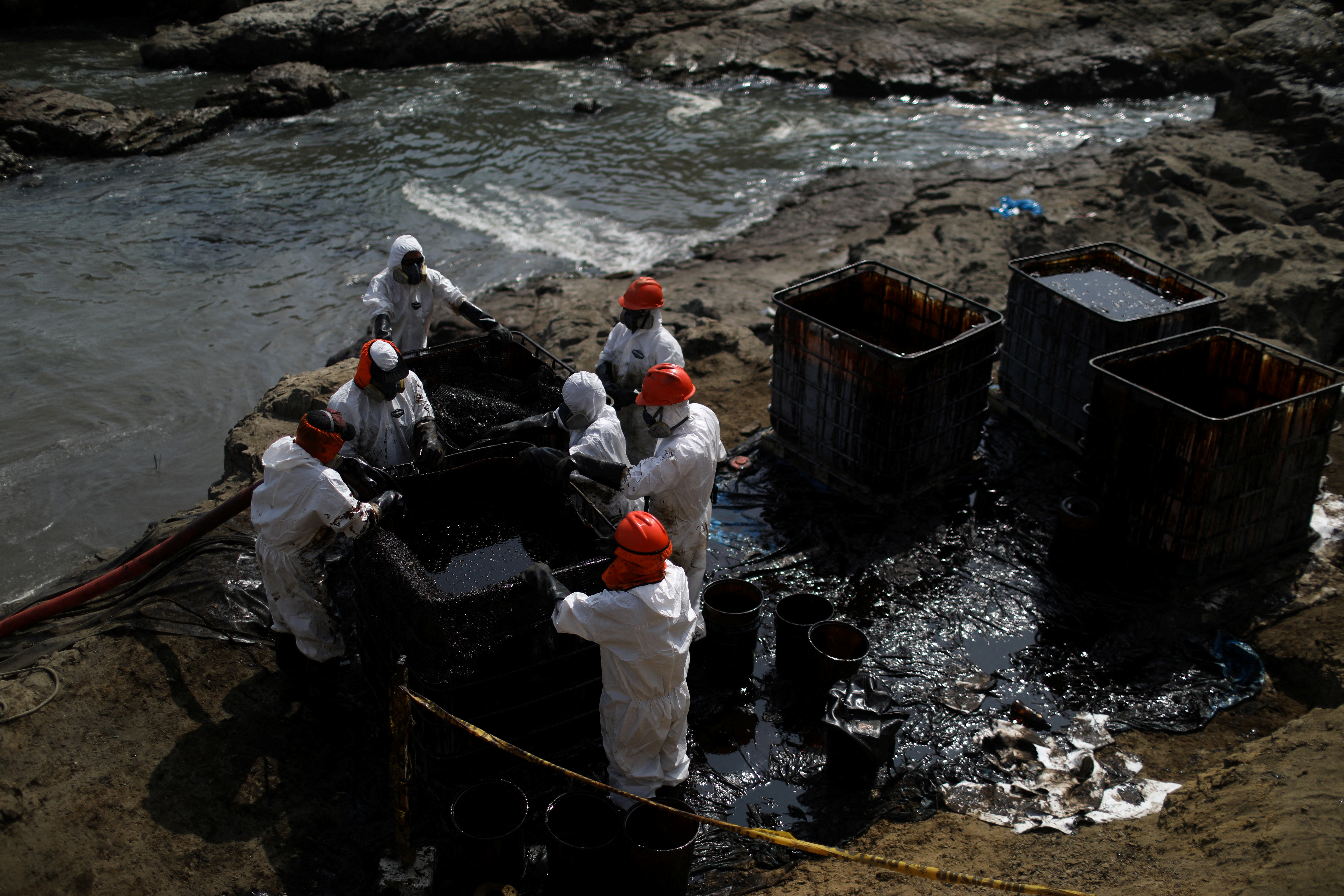 Workers clean up an oil spill following an underwater volcanic eruption, in Ventanilla