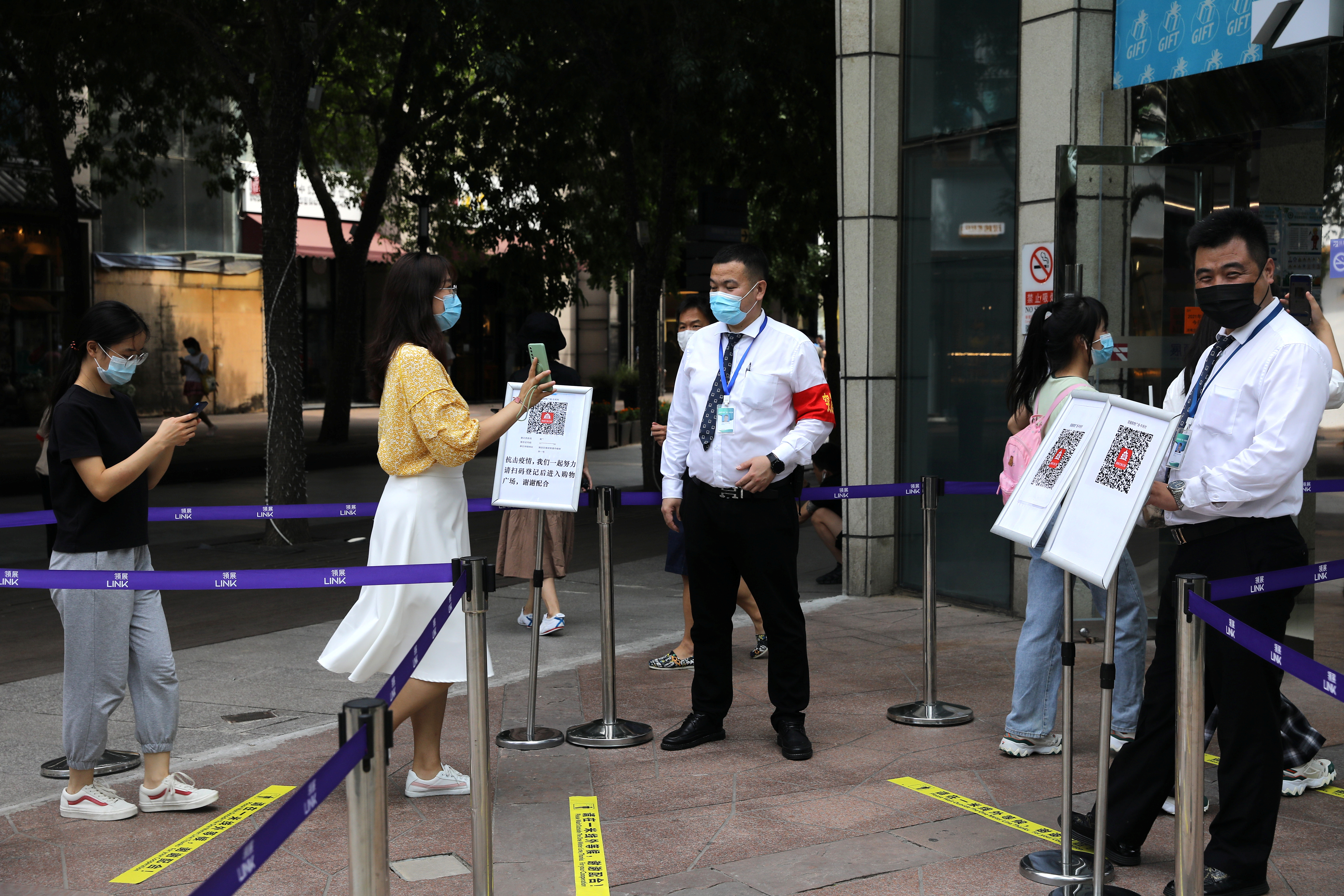 Woman shows her health status on a phone to a security guard, at an entrance of a shopping mall in Beijing