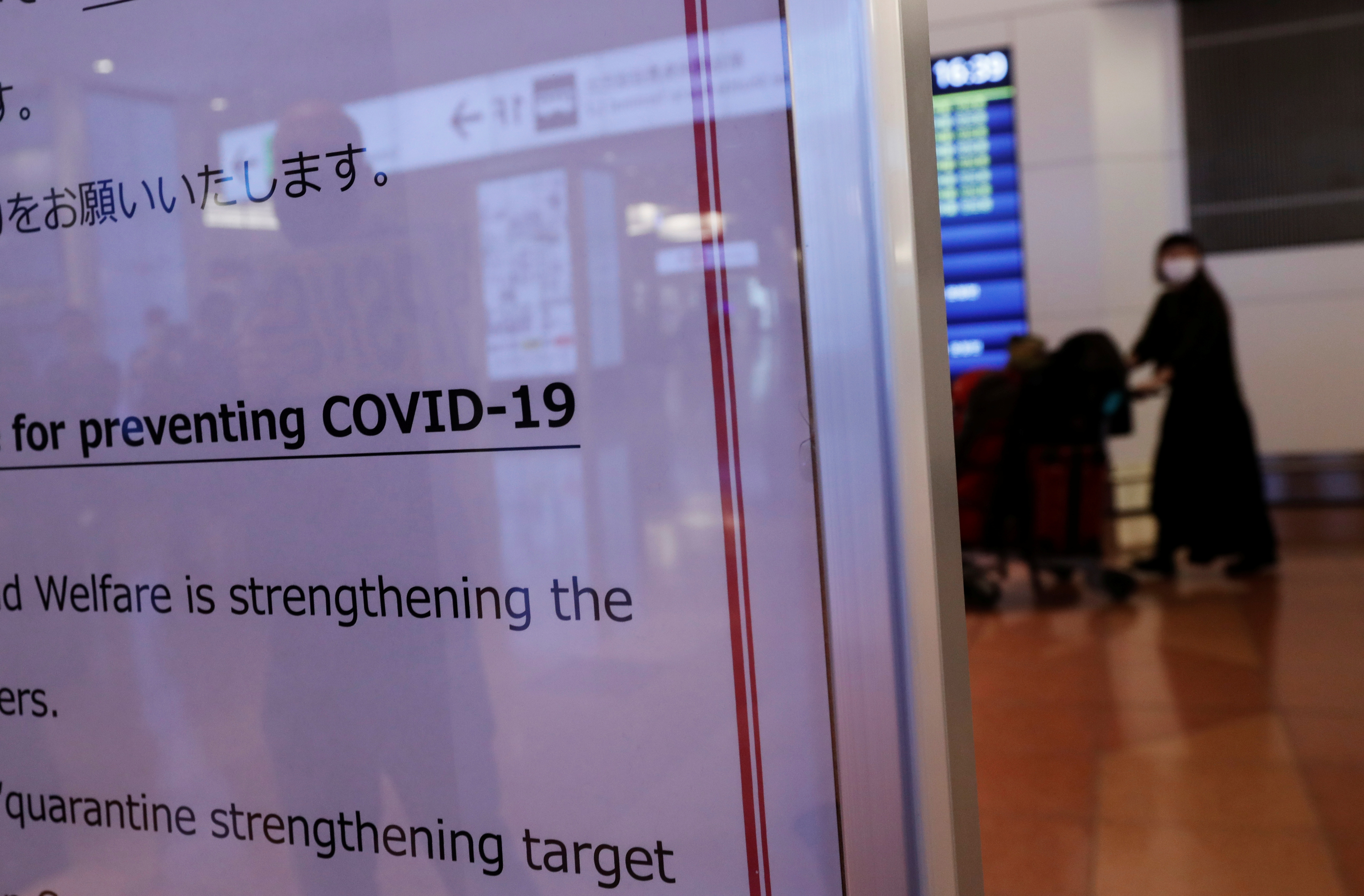 A passenger is seen behind a notice about the coronavirus disease (COVID-19) measurements at an arrival hall of Haneda airport's international terminal, amid the coronavirus disease (COVID-19) outbreak, in Tokyo