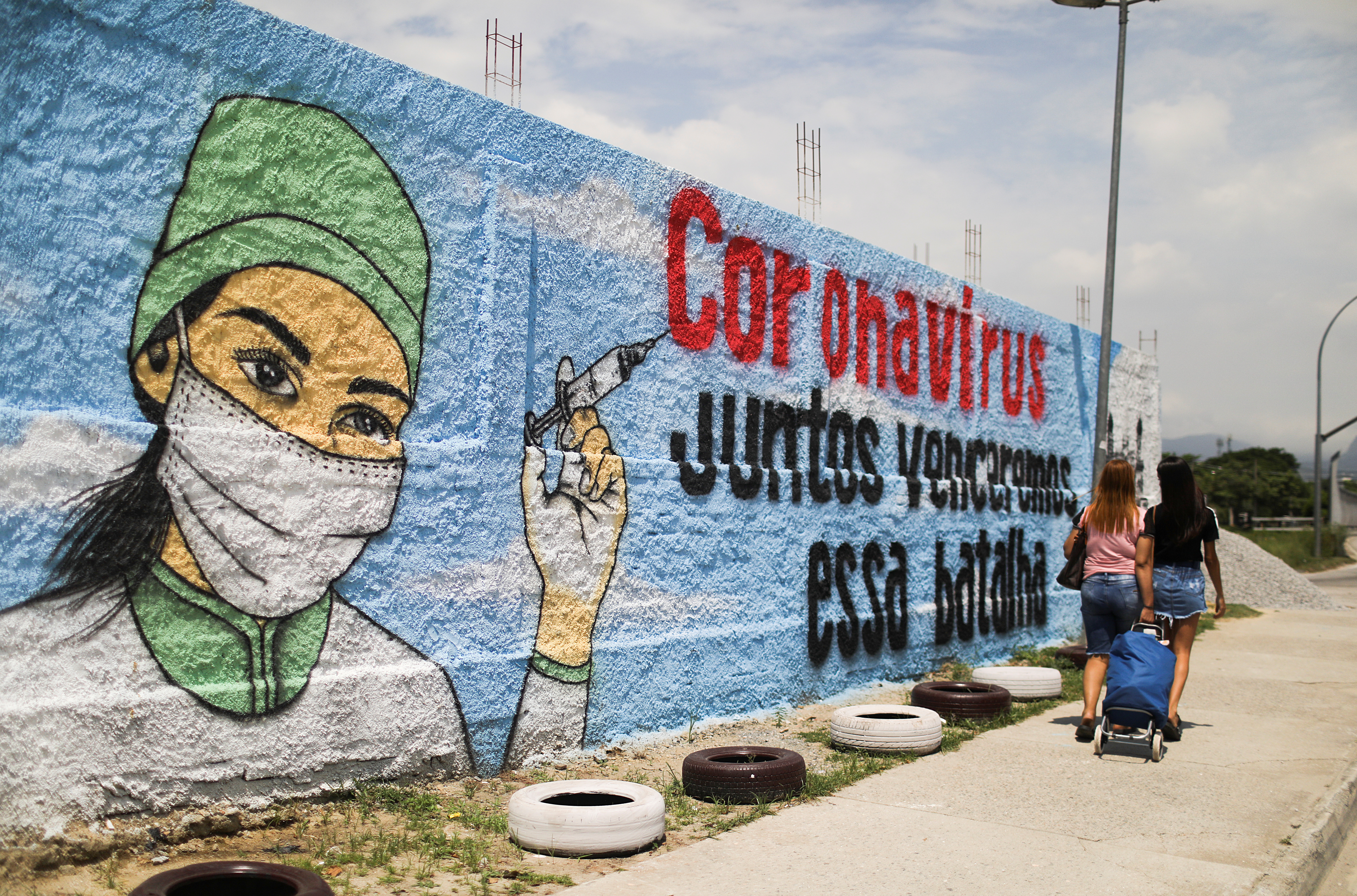 People walk past a graffiti amidst the spread of the coronavirus disease (COVID-19) in Rio de Janeiro, Brazil March 12, 2021. The graffiti reads: "Coronavirus, together we will win that battle". REUTERS/Pilar Olivares