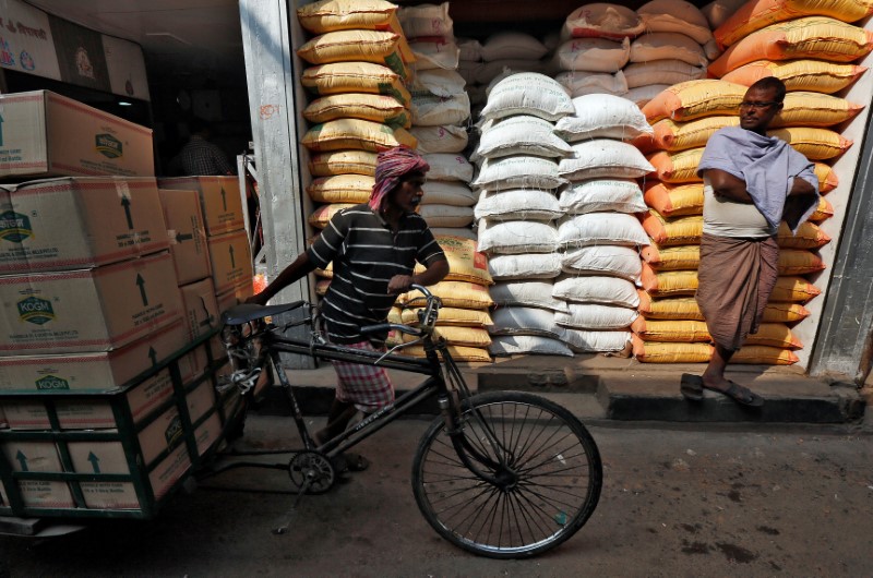 A labourer carries vegetable oil packets on a tricycle as a man stands in front of his shop selling food grains, at a wholesale market in Kolkata