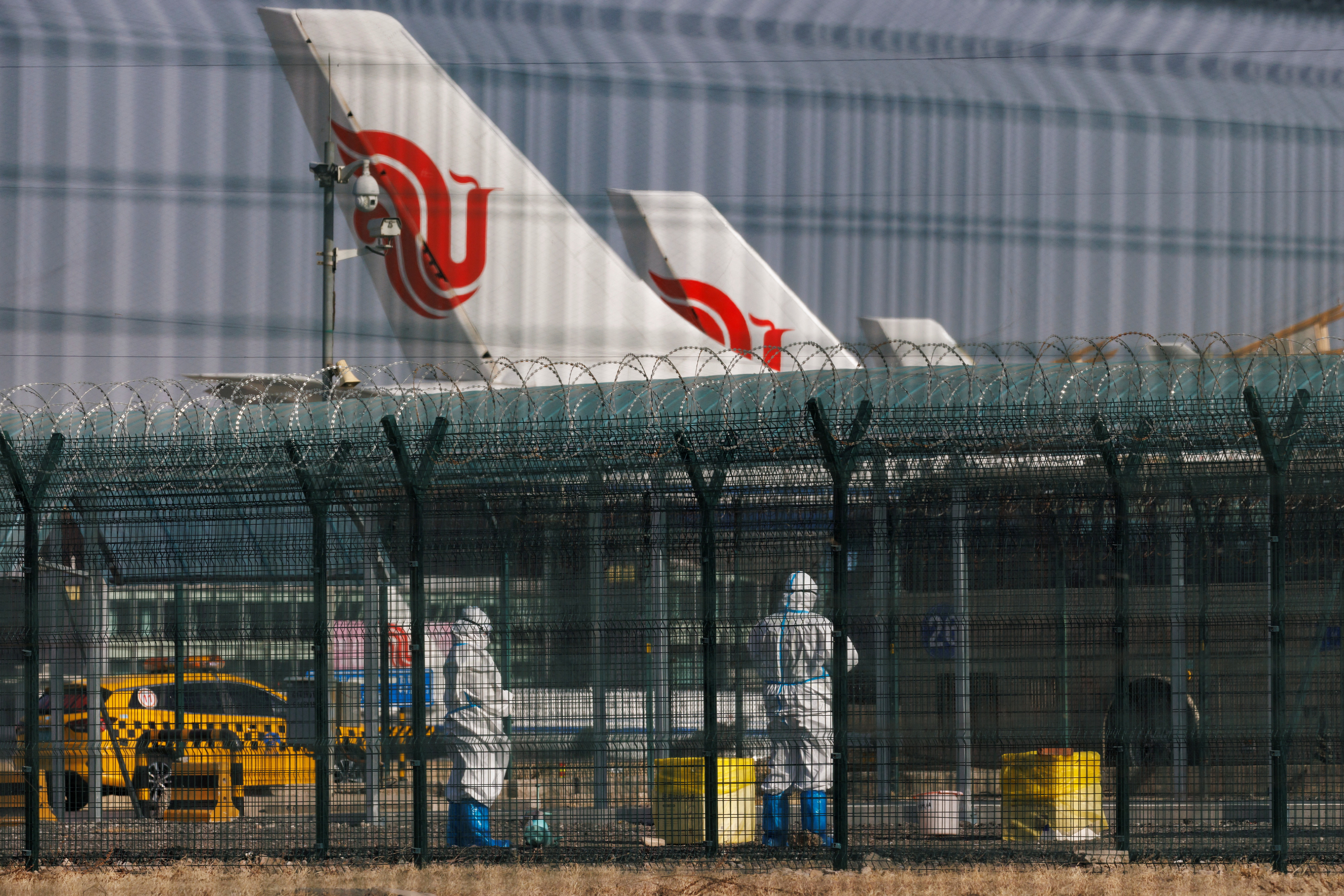 Workers in protective suits stand near planes of Air China airlines at Beijing Capital International Airport as coronavirus disease (COVID-19) outbreaks continue in Beijing