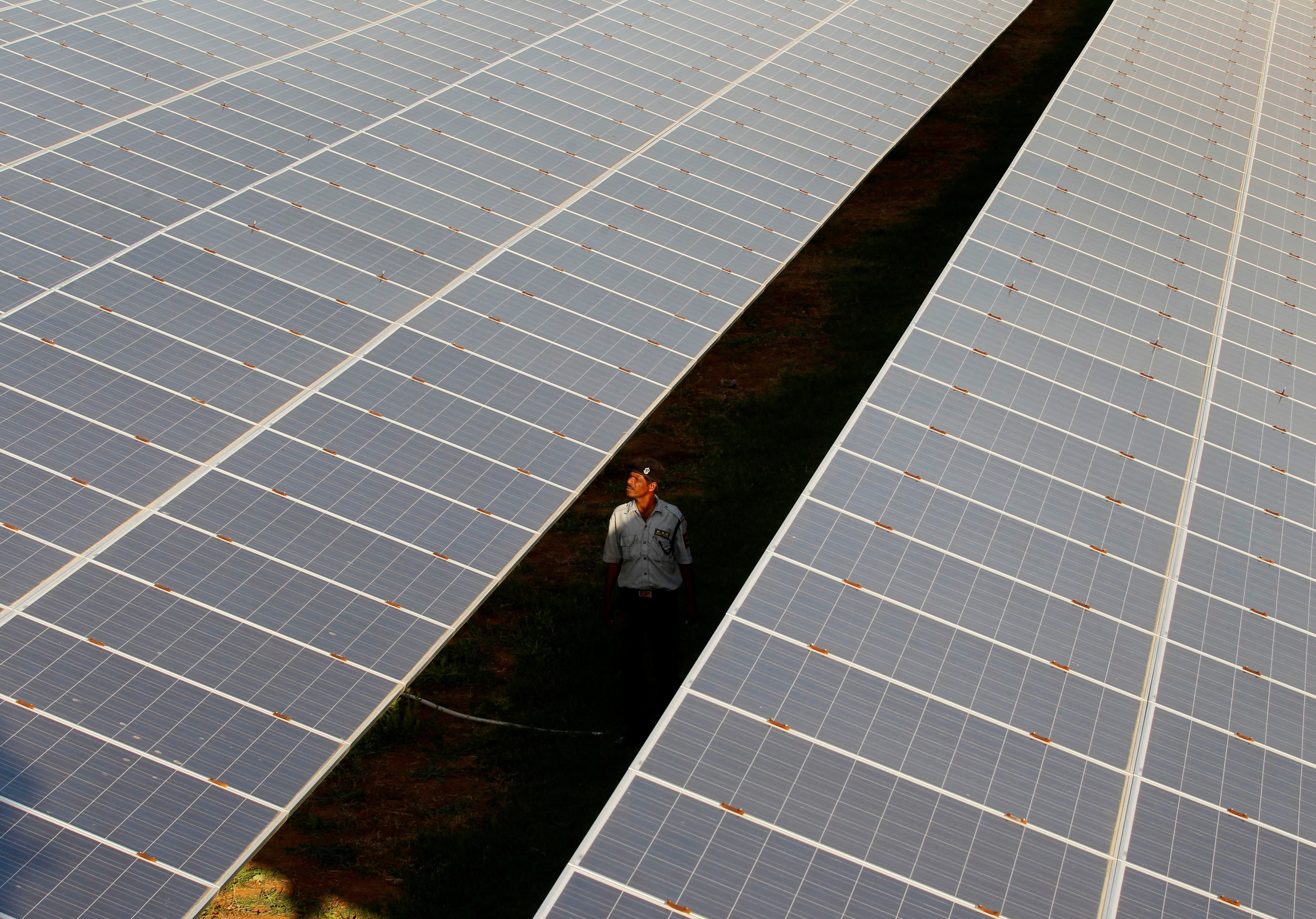 A private security guard walks between rows of photovoltaic solar panels inside a solar power plant at Raisan