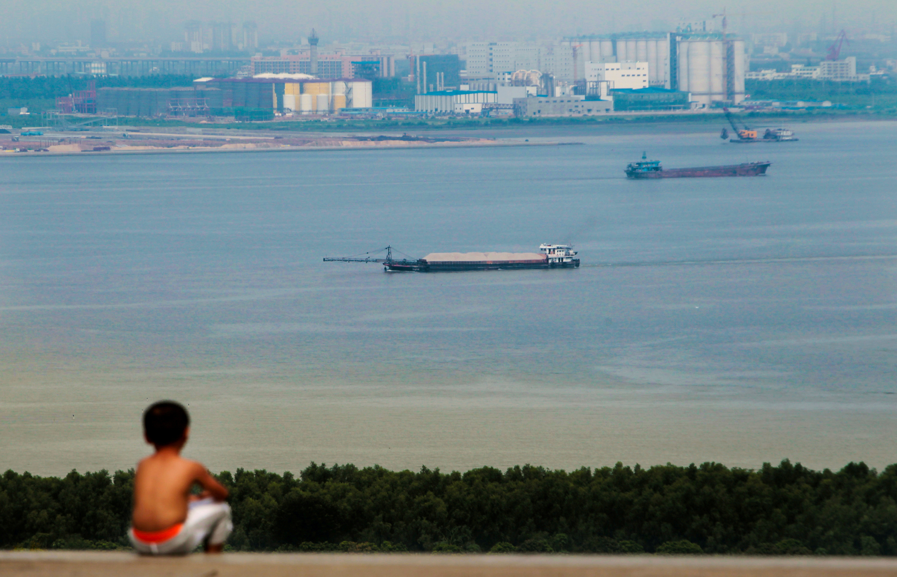 Boy looks at cargo ships passing along the Pearl River in Guangzhou, Guangdong province