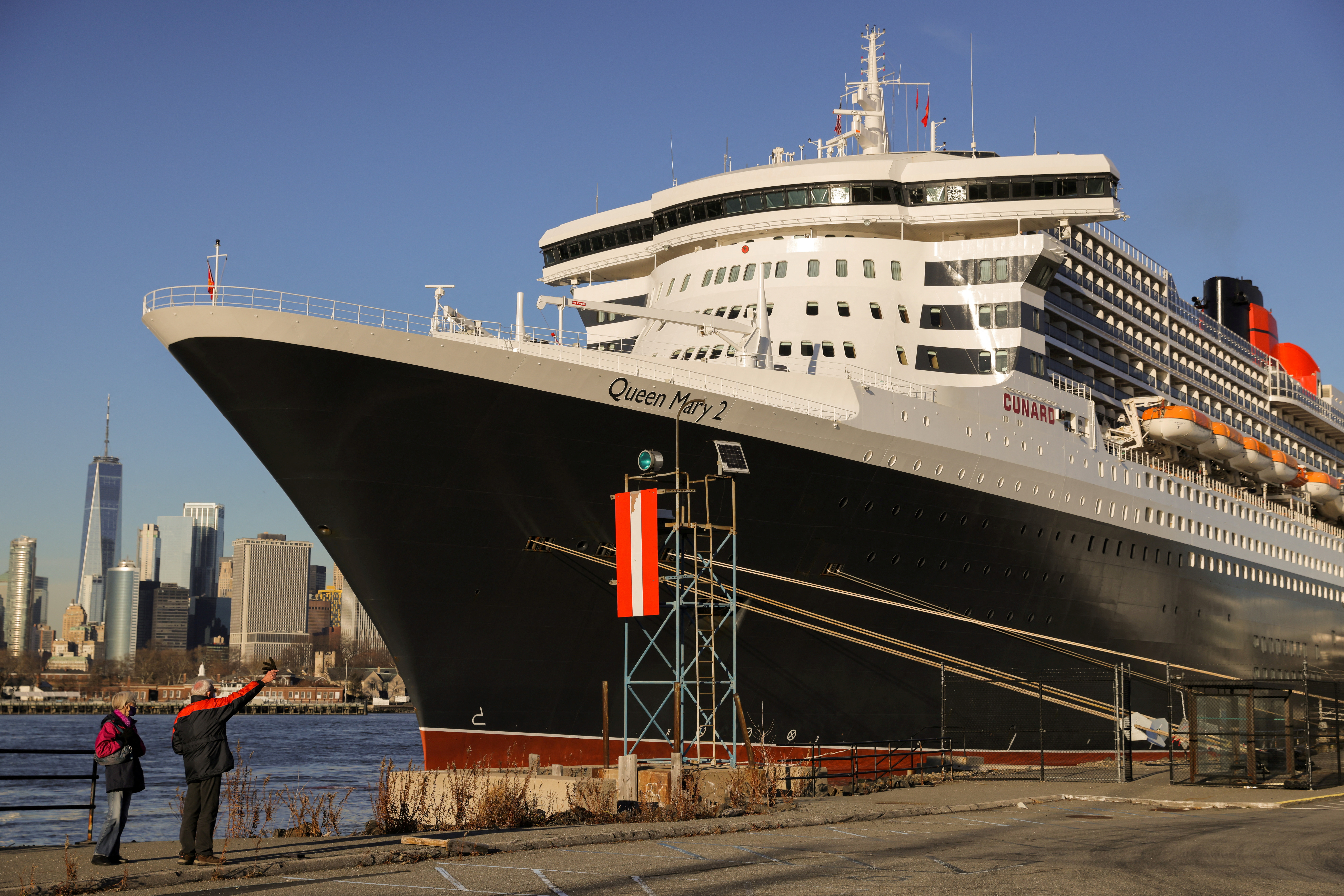 People look toward the Queen Mary 2 cruise ship by Cunard Line, owned by Carnival Corporation & plc. as it sits docked at Brooklyn Cruise Terminal in Brooklyn, New York City
