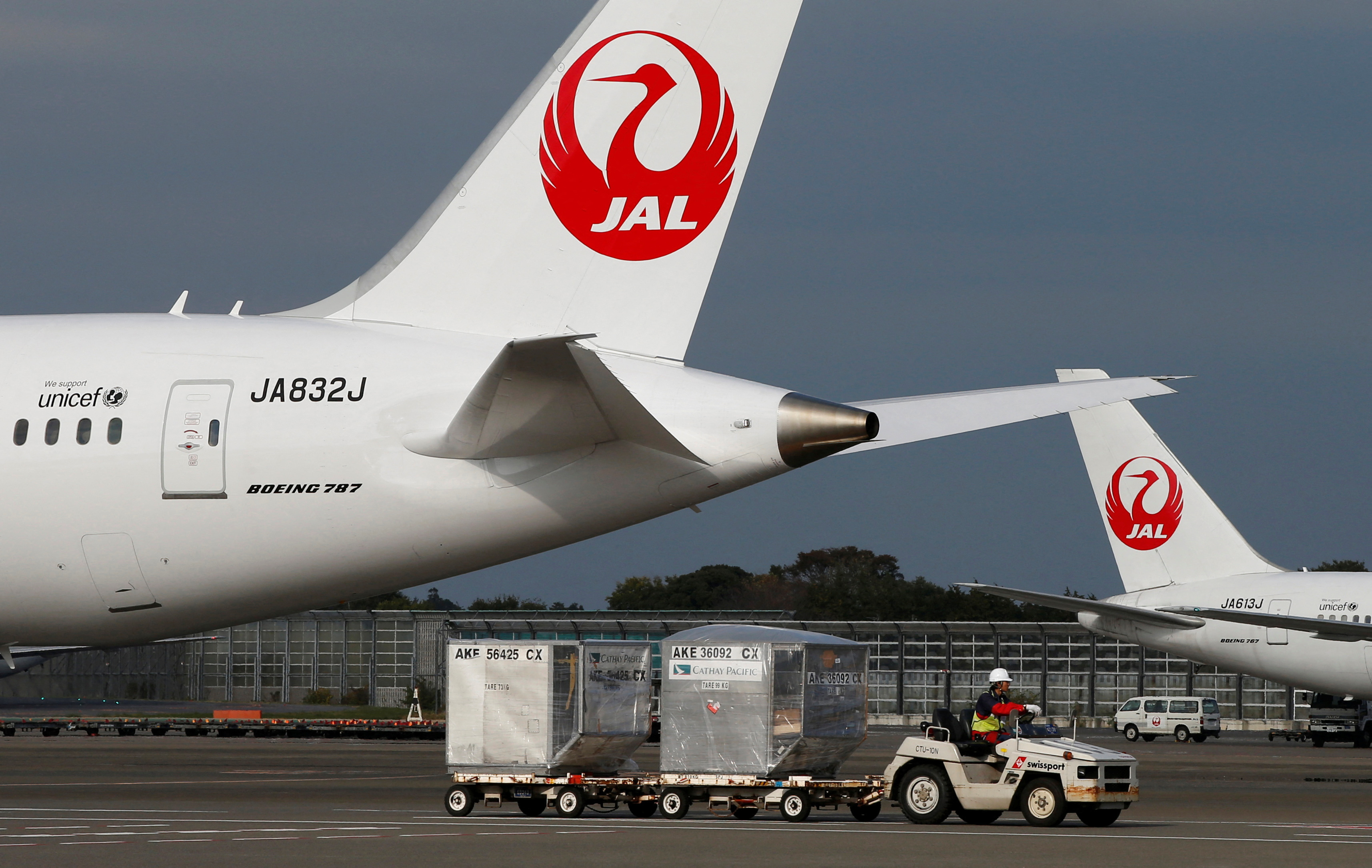 A airport worker drives a luggage transport vehicle past one of the company's Boeing Co's 787 Dreamliner plane and a Beoing 767 at Narita international airport in Narita