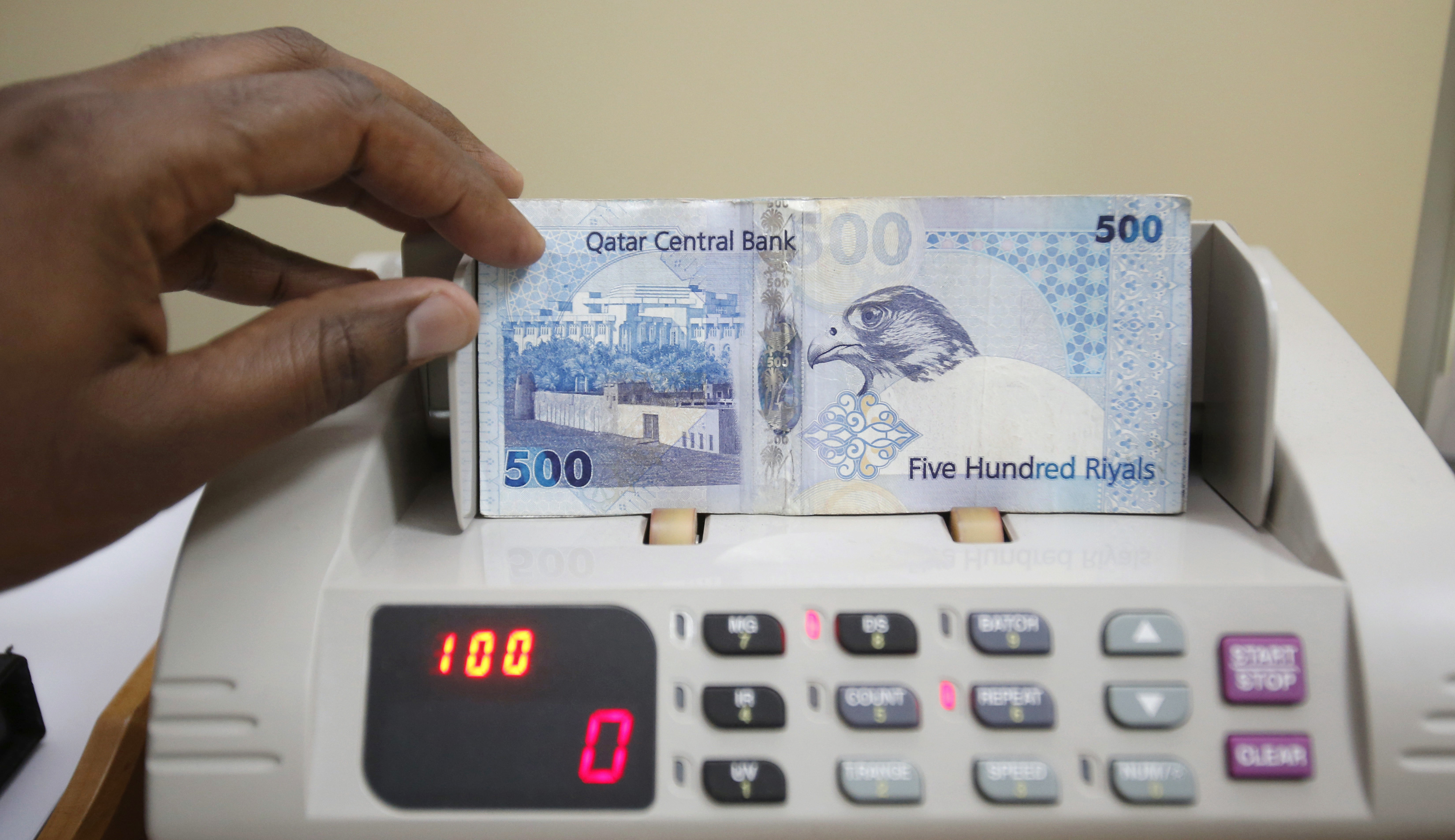 cashier counts Qatari riyal notes at a money changer in Doha