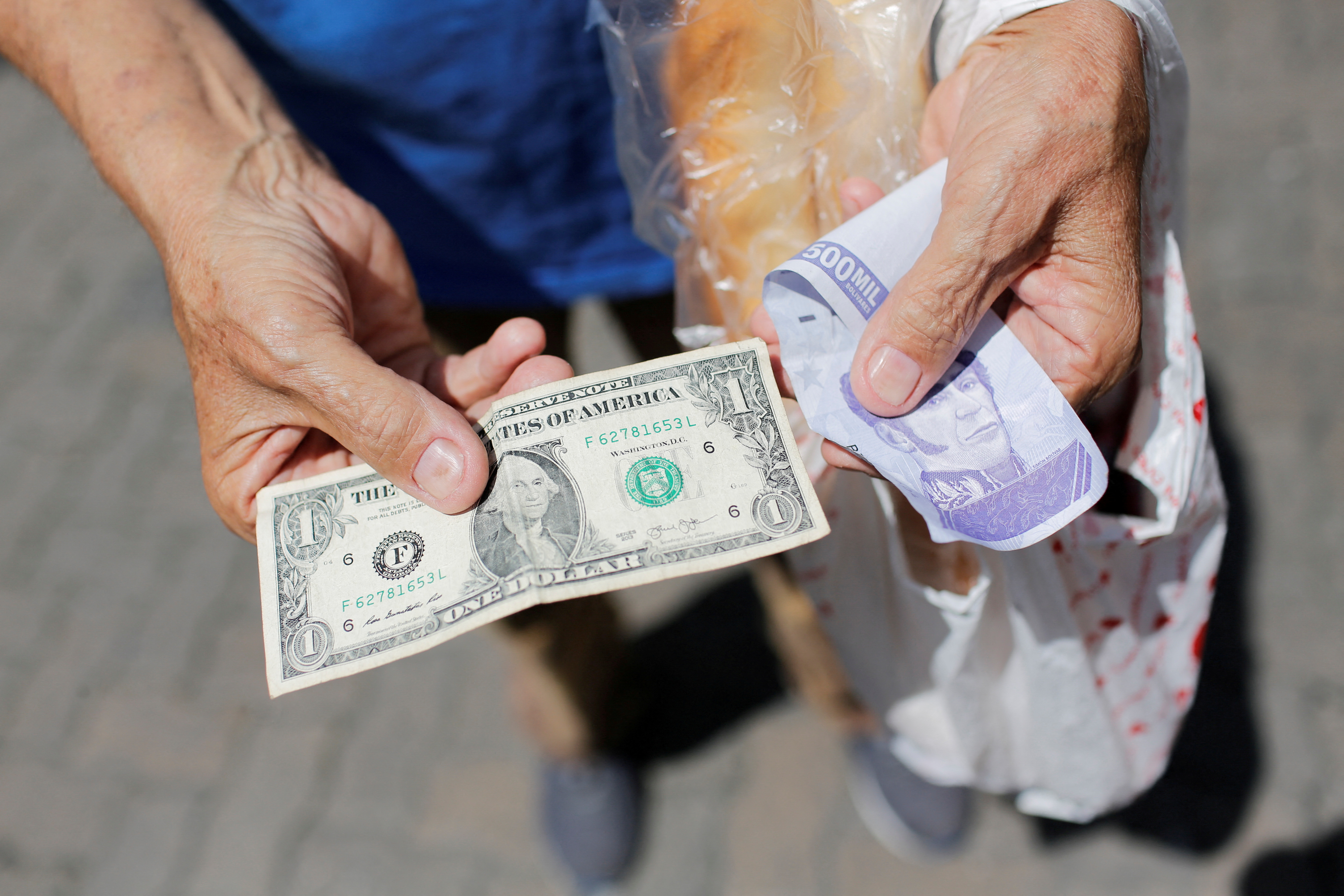 A street vendor holds a one dollar banknote beside an old Bolivar banknote in Caracas