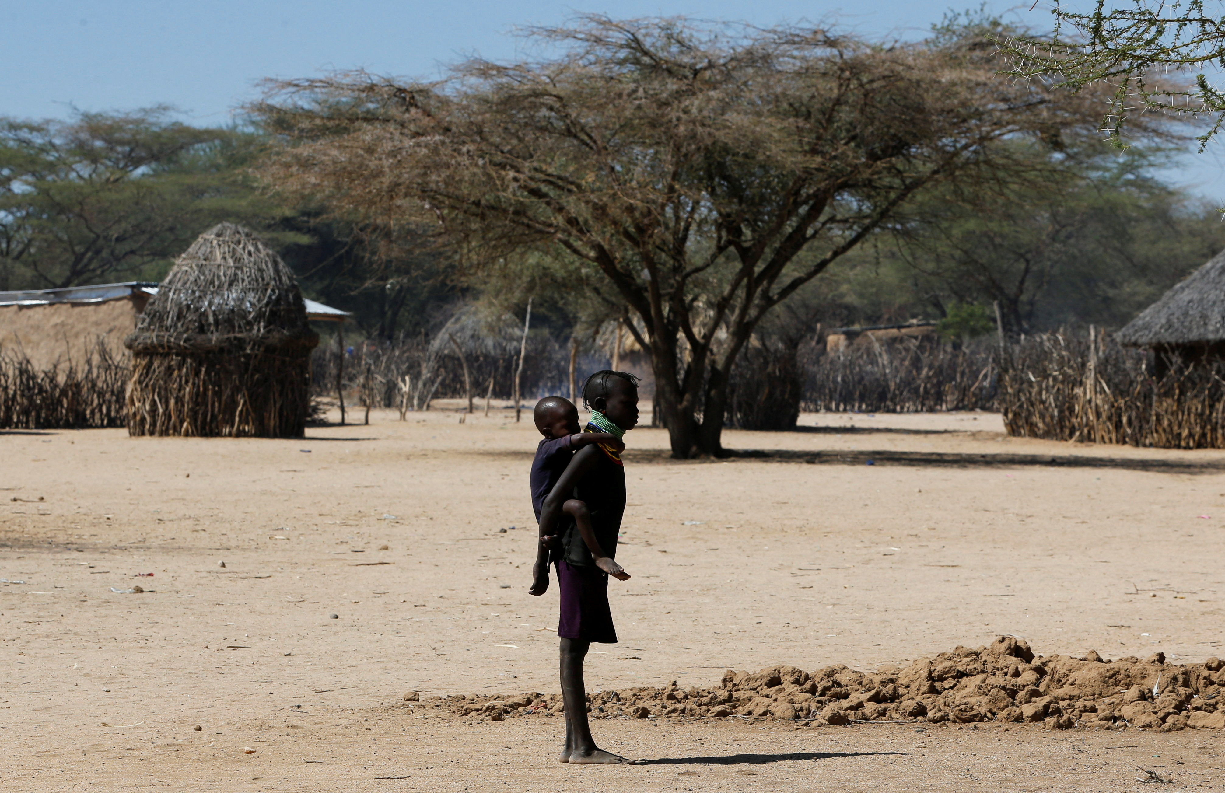 A child affected by the worsening drought due to failed rain seasons, carries her sibling as they stand near their makeshift shelter at Sopel village in Turkana