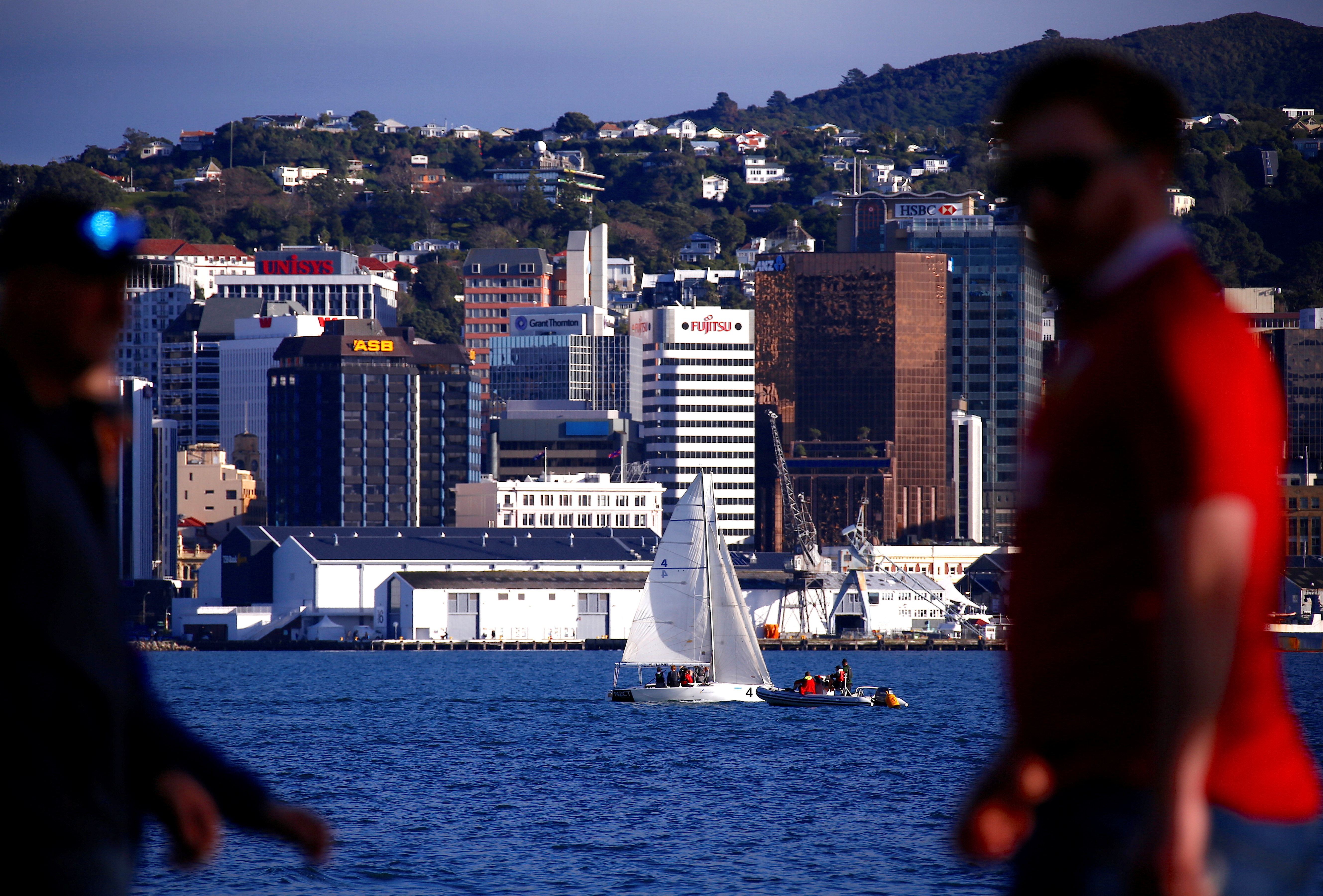 Pedestrians walk past a sailing boat as it passes in front of the central business district of Wellington in New Zealand