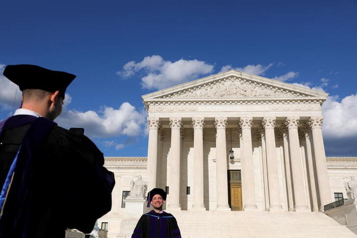Graduates from The George Washington University Law School take photos in their graduation regalia outside the United States Supreme Court Building in Washington, D.C.