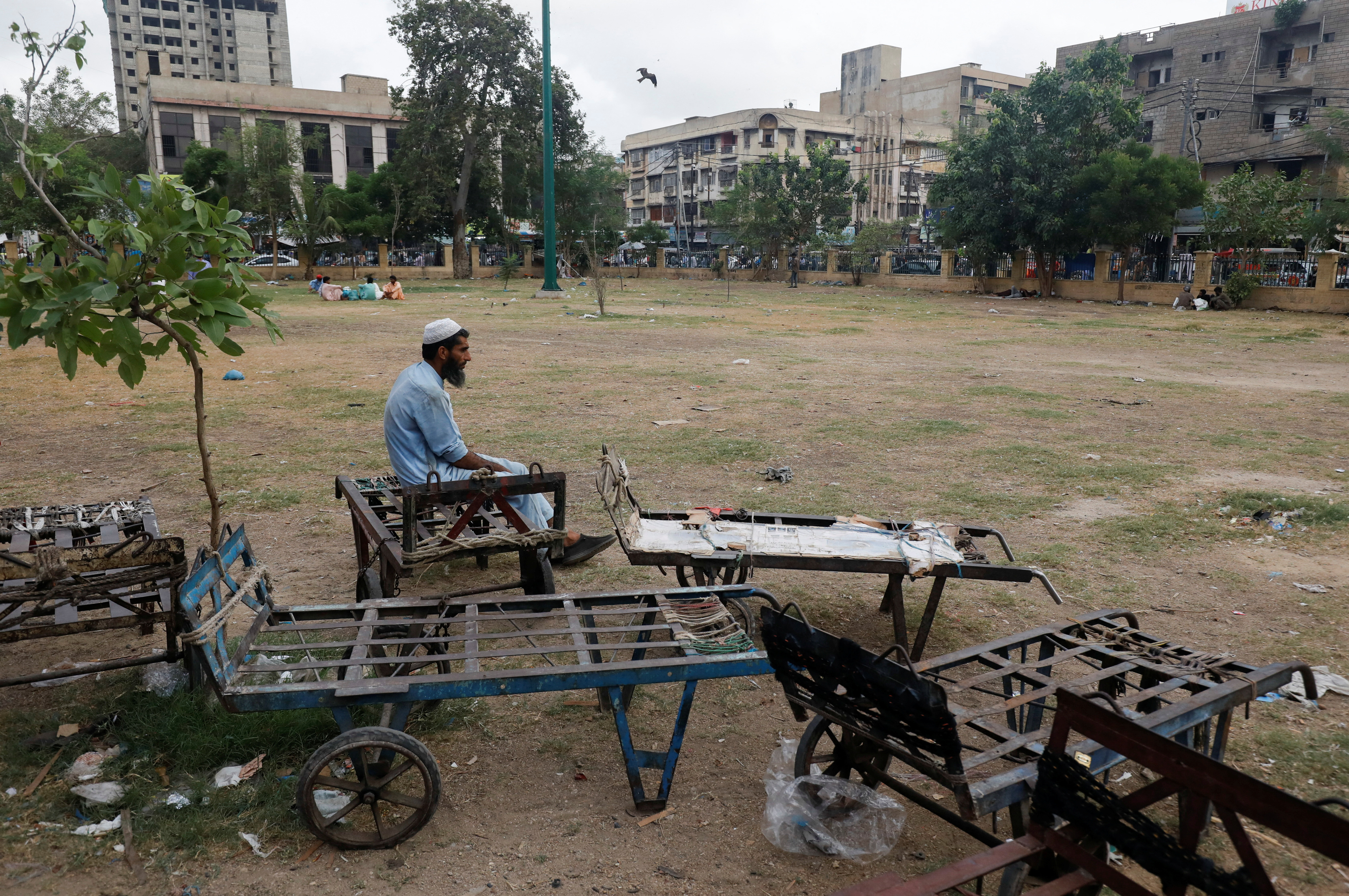 Labourer waits for work while sitting beside push trollies outside a market in Karachi