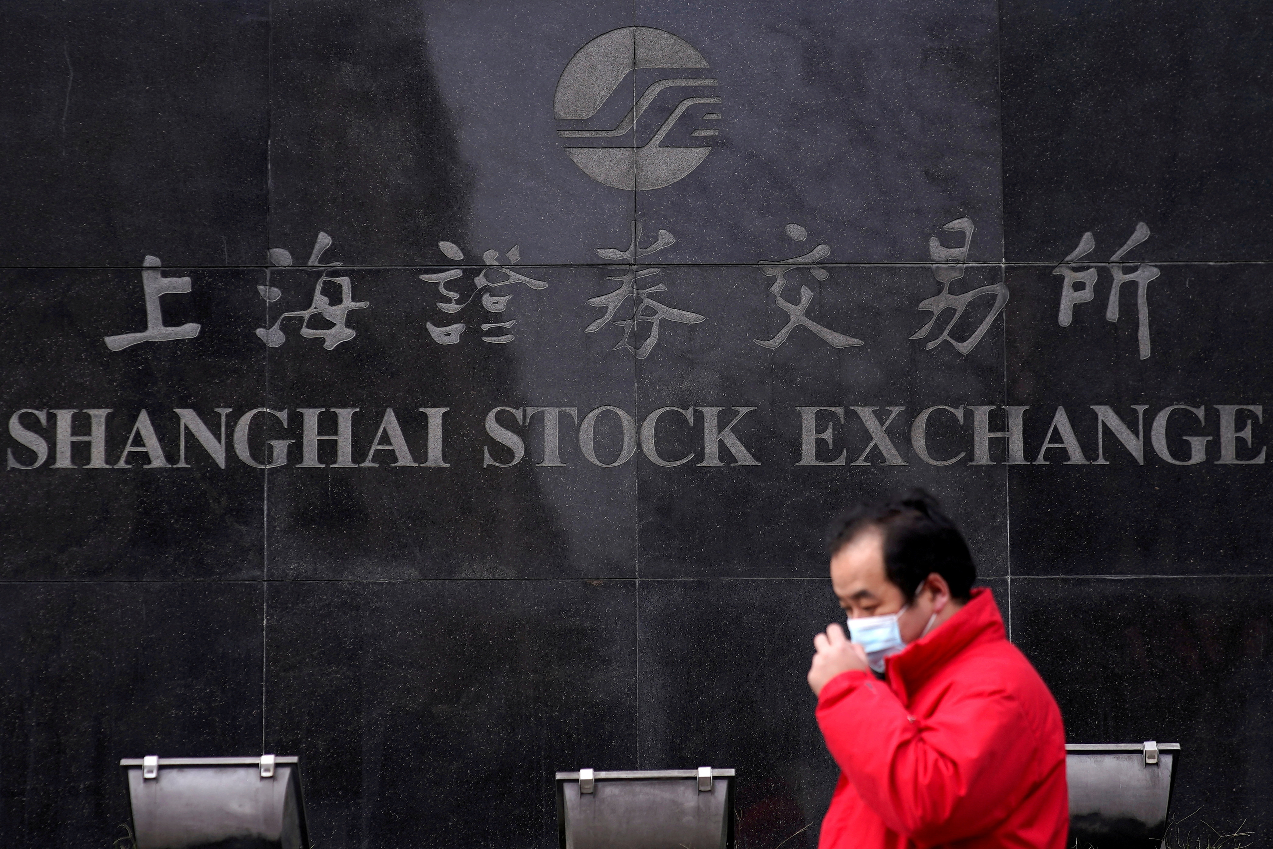 A man wearing a mask walks by the Shanghai Stock Exchange building at the Pudong financial district in Shanghai