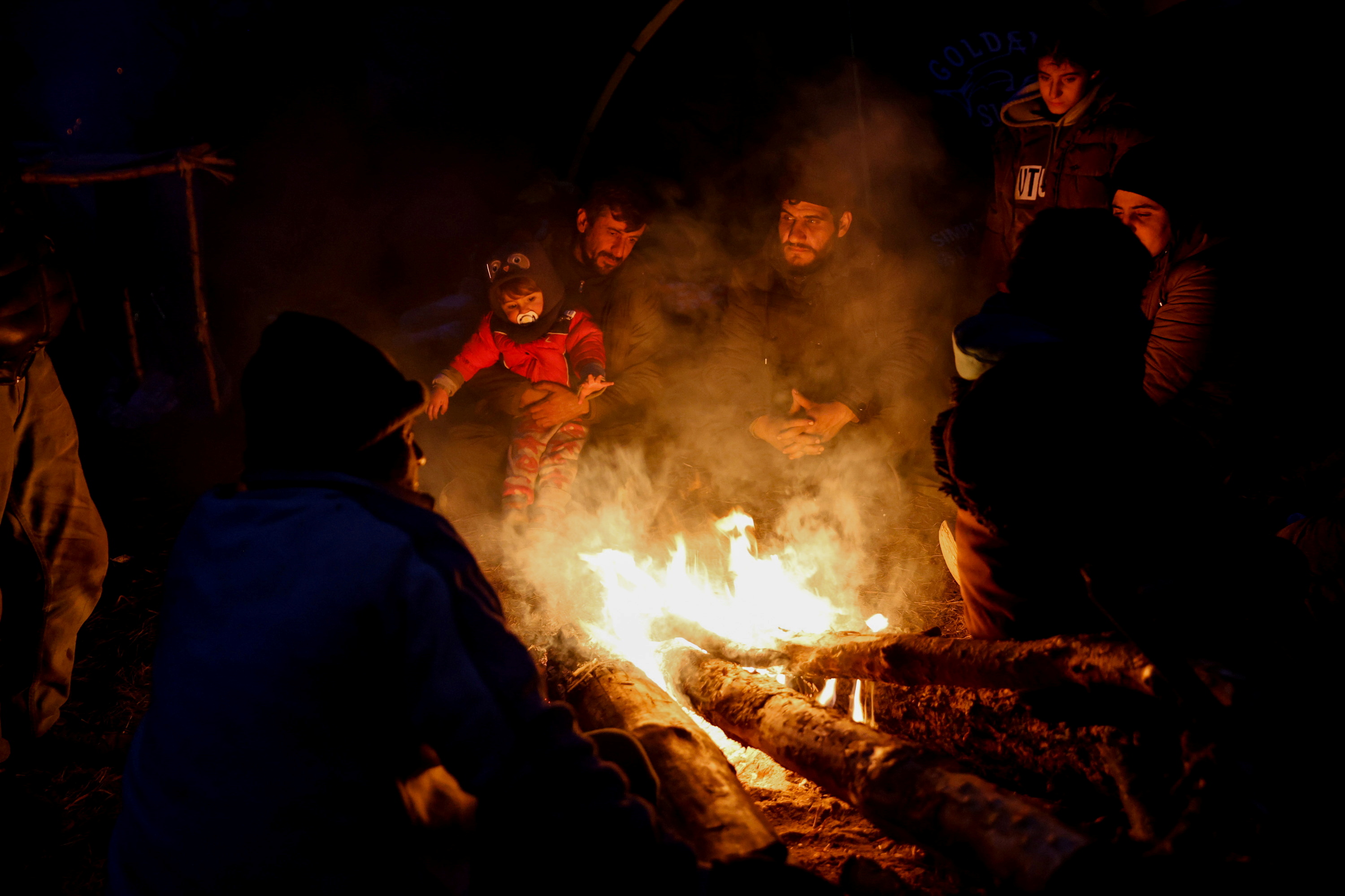 Migrants gather around a fire in a temporary camp on the Belarusian-Polish border in the Grodno region, Belarus 14 November 2021. Photo taken 14 November 2021. Oksana Manchuk / BelTA / Handout via REUTERS 