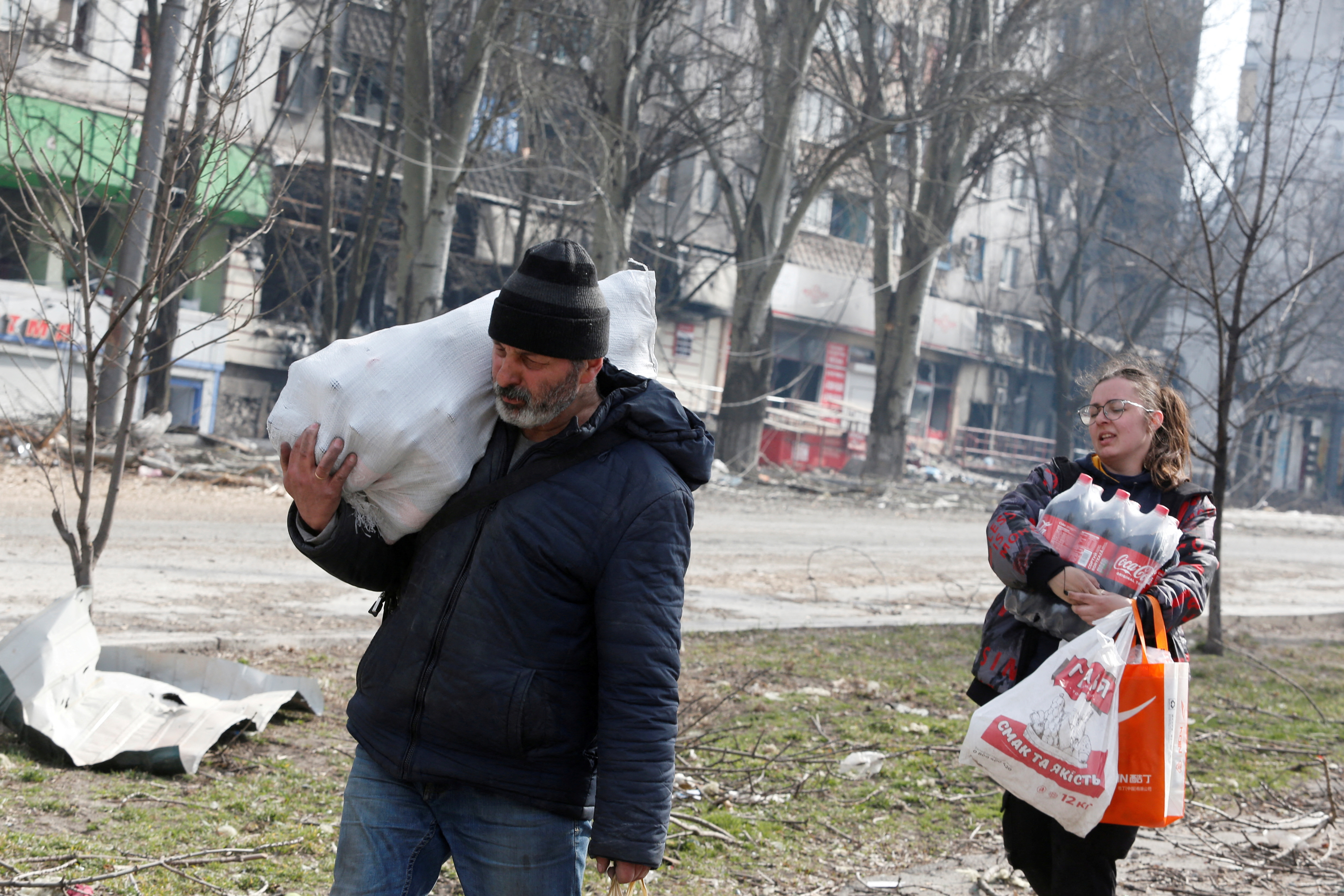 Local residents carry foodstuff while walking past a damaged apartment building in Mariupol