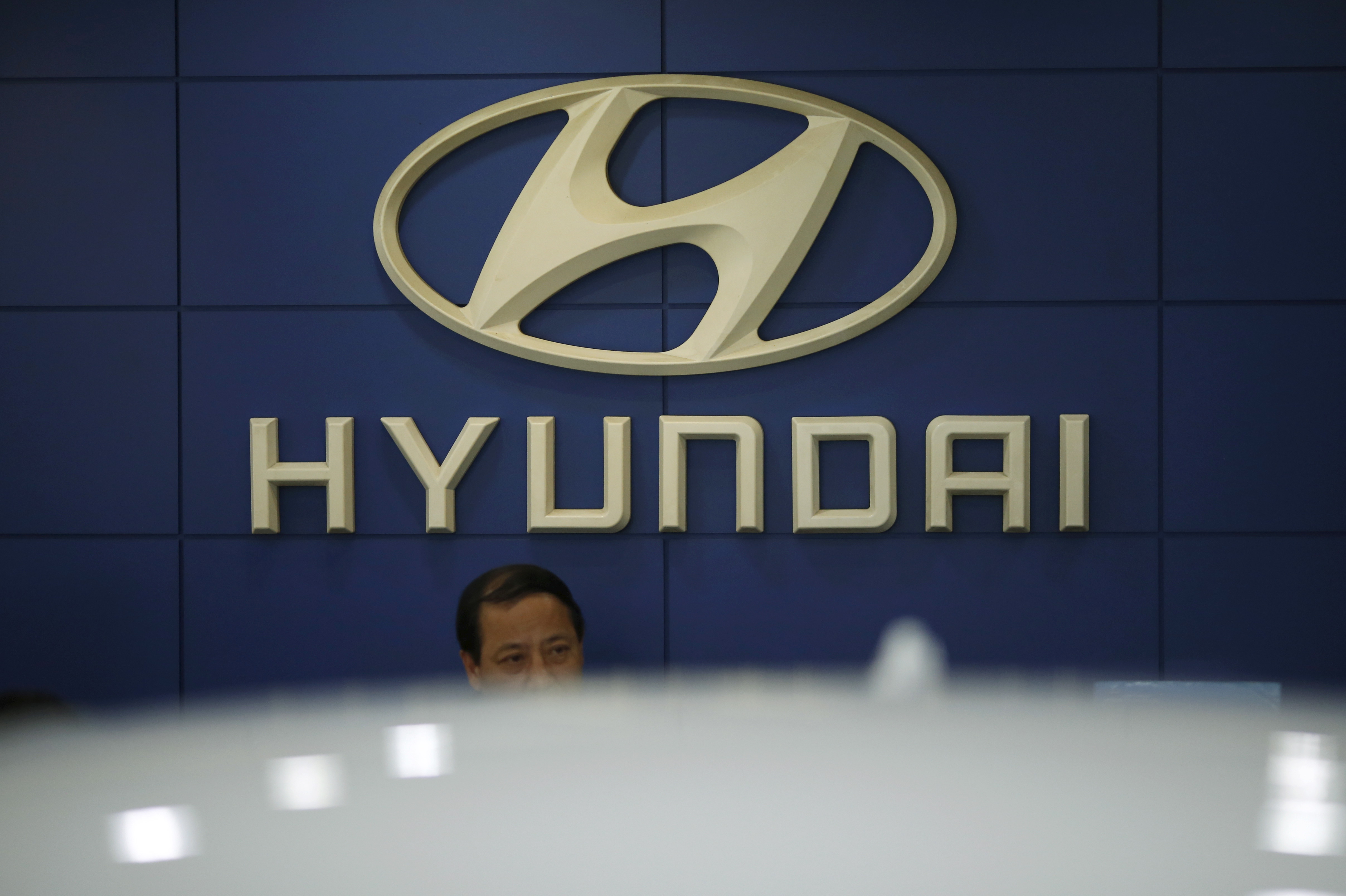 An employee sits in front of the logo of Hyundai Motor Co. at its dealership in Seoul